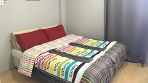 Una cama con una colcha a rayas de colores y almohadas rojas, una cortina gris y una cita motivacional en la pared.