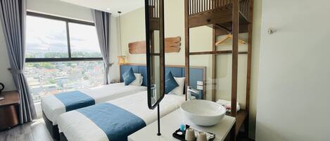 A hotel room with two beds, a large window with curtains, a wooden headboard, a mirror, a sink, and a tray with toiletries.
