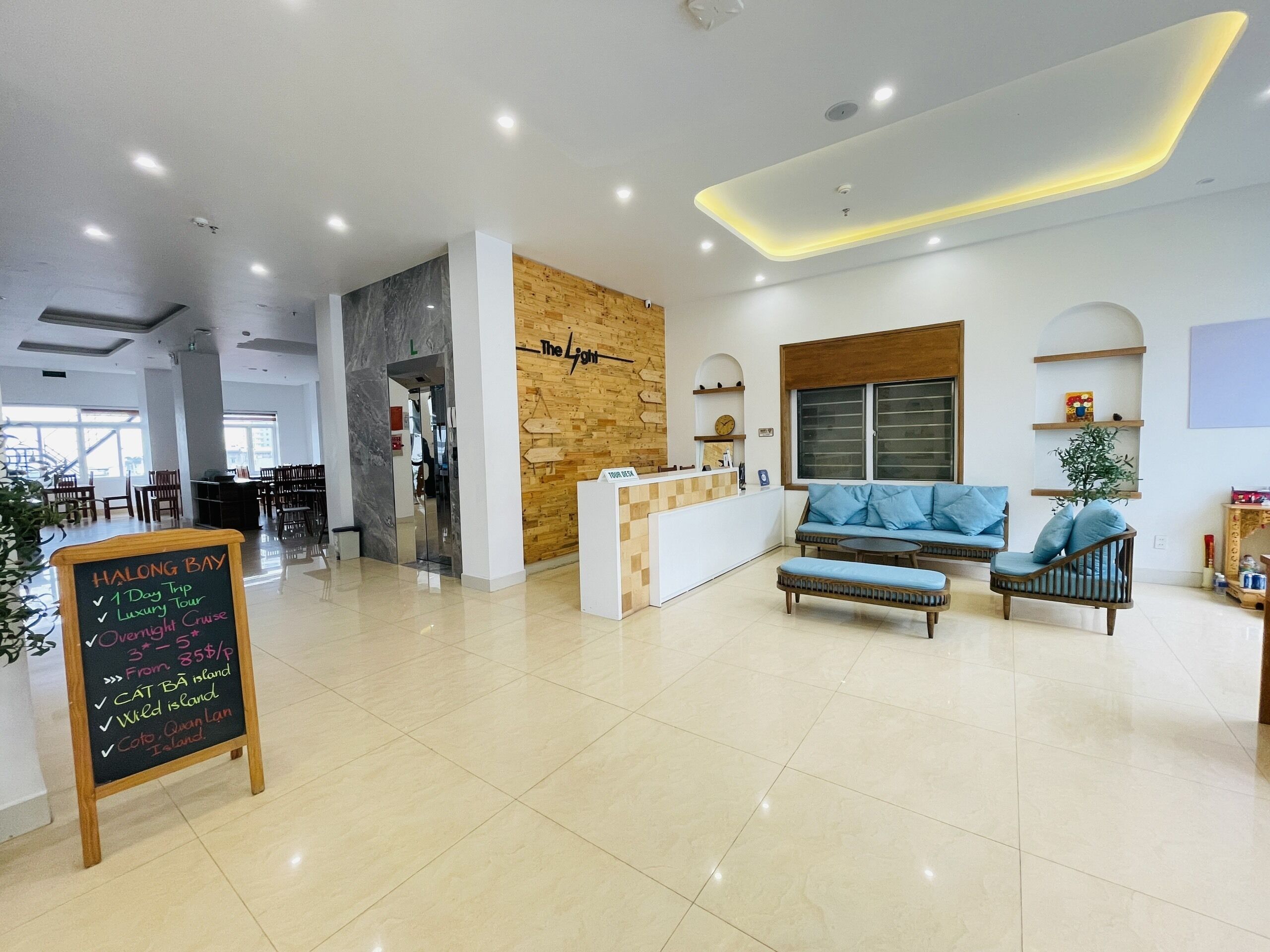 A modern hotel lobby with a reception desk, seating area, and a chalkboard sign detailing tour options.