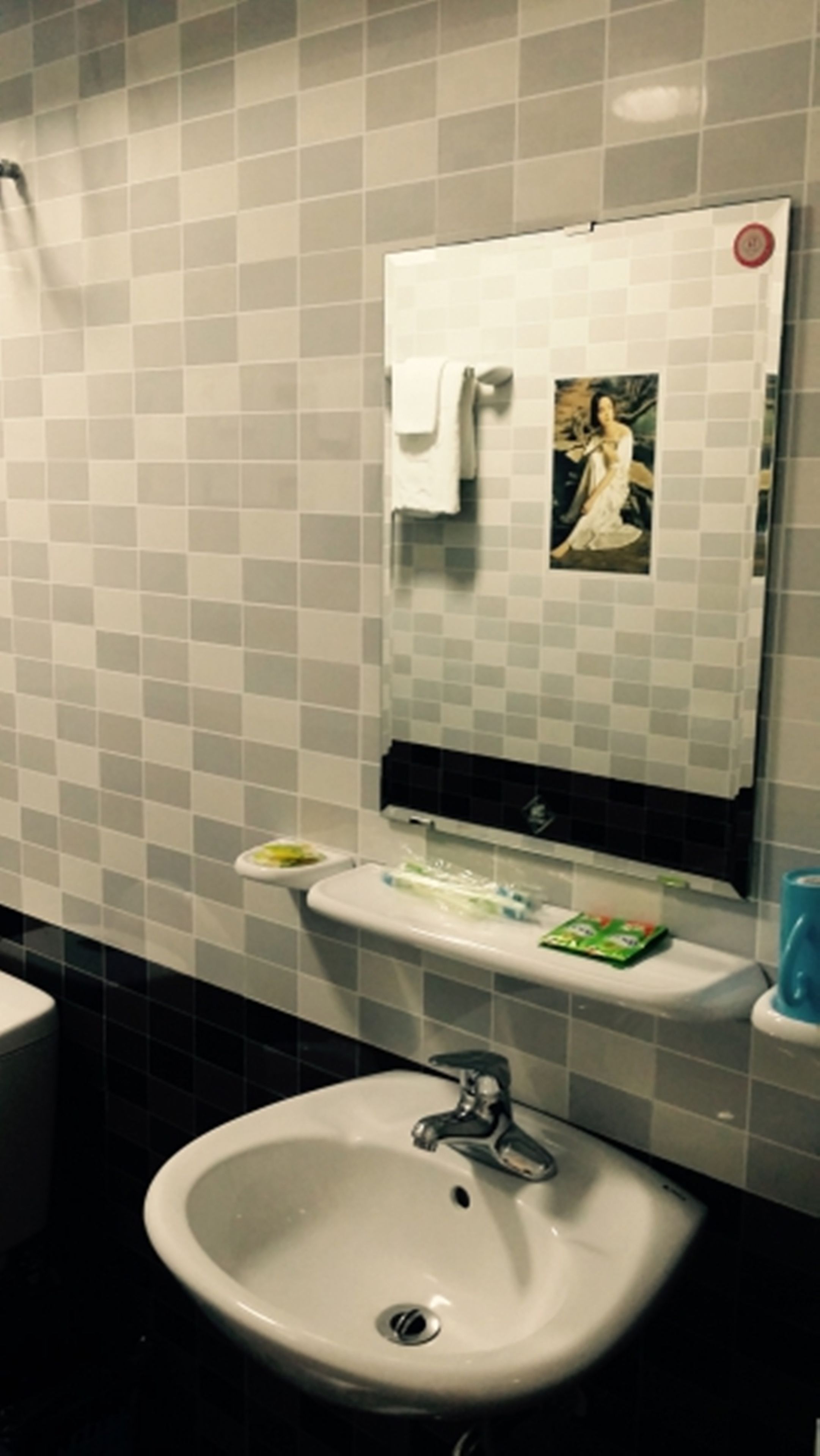 Et badeværelse med en hvid vask, et spejl med et håndklæde og en lille hylde med toiletartikler.