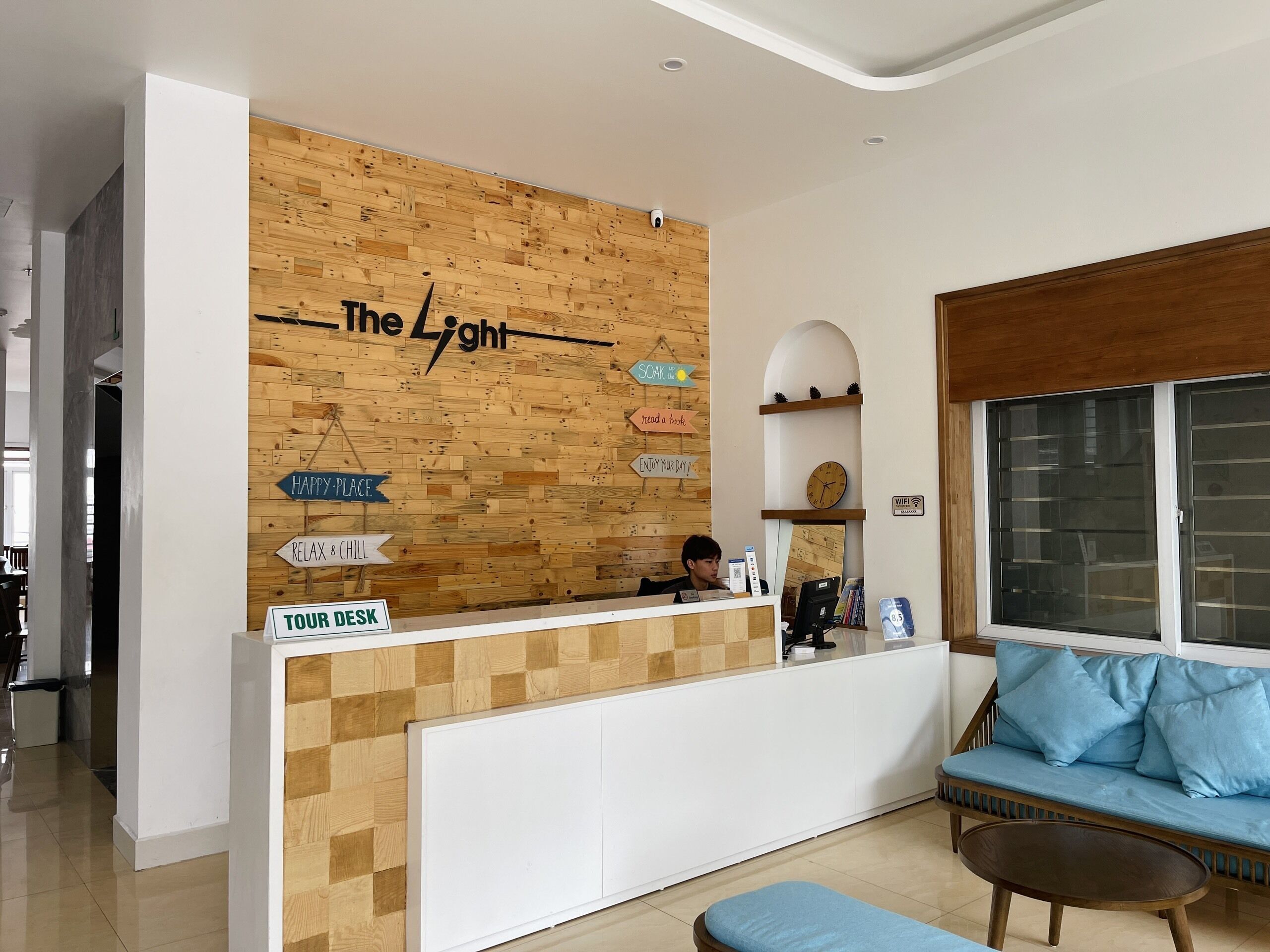 A reception desk with a wooden wall and signs, a sofa, and a window with blinds.