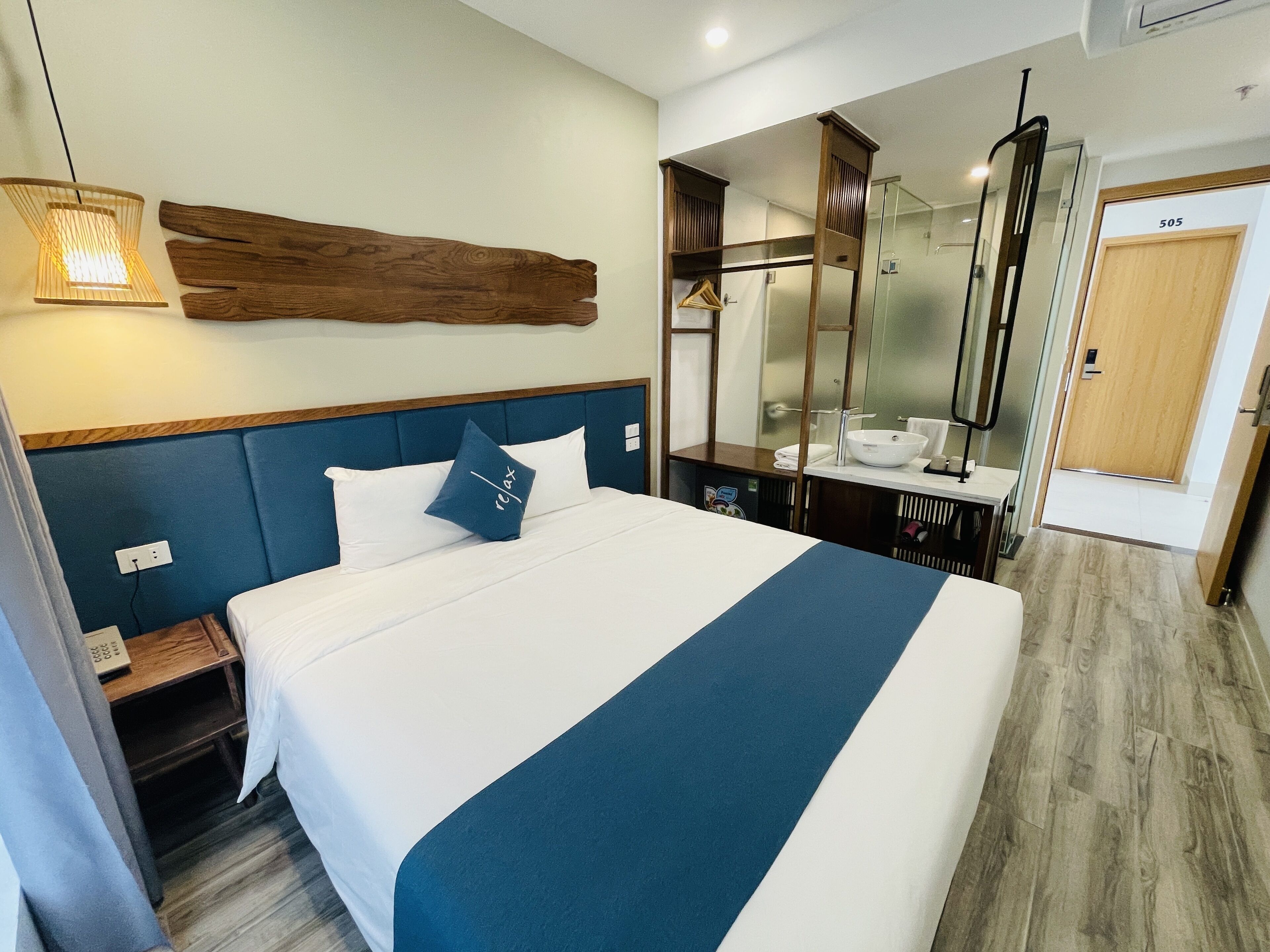 A hotel room with a large bed, a wooden headboard, a nightstand, a bathroom with a mirror, and a door labeled 505.