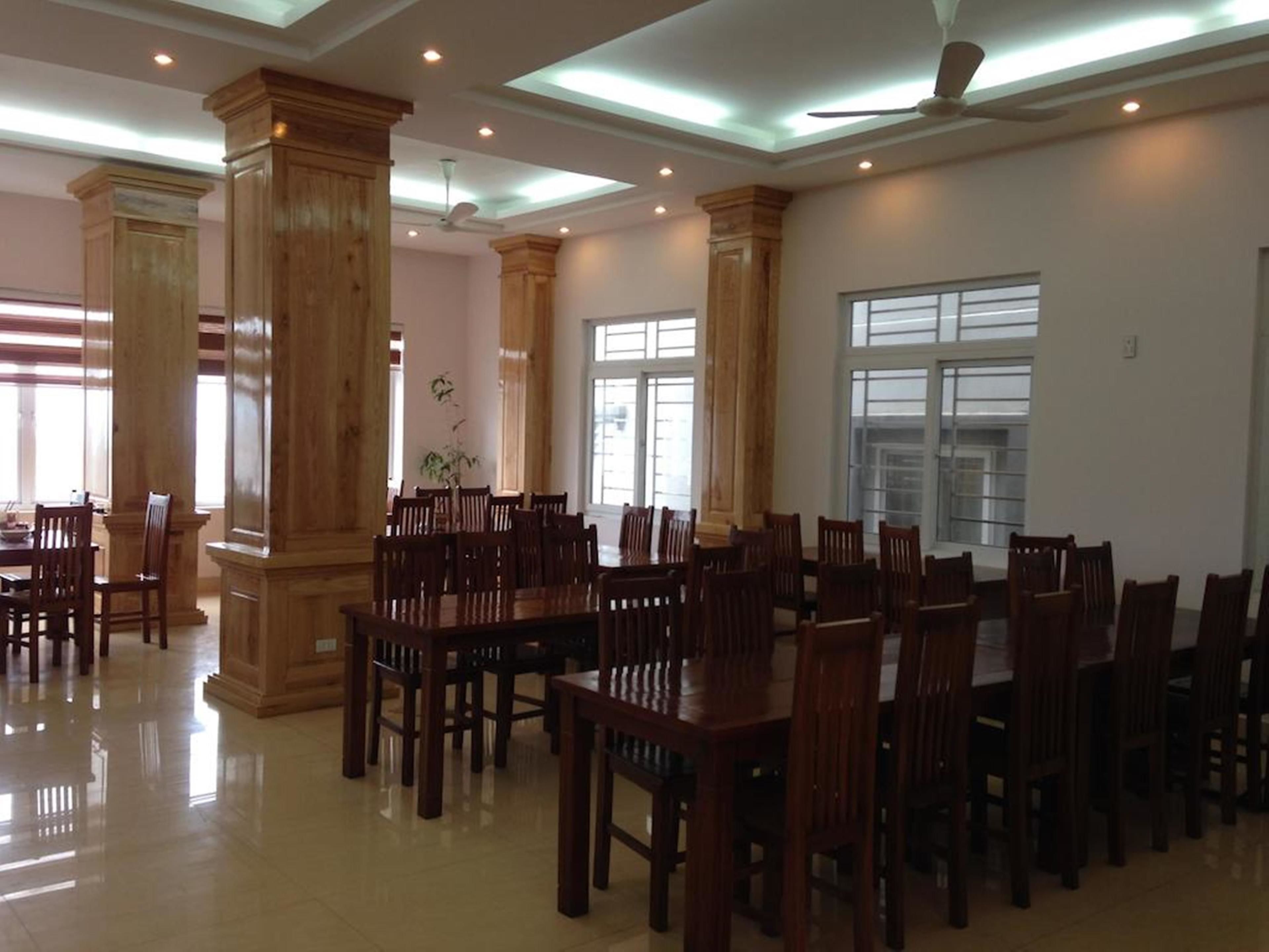 A spacious dining area with wooden tables and chairs, large windows, and a ceiling fan.