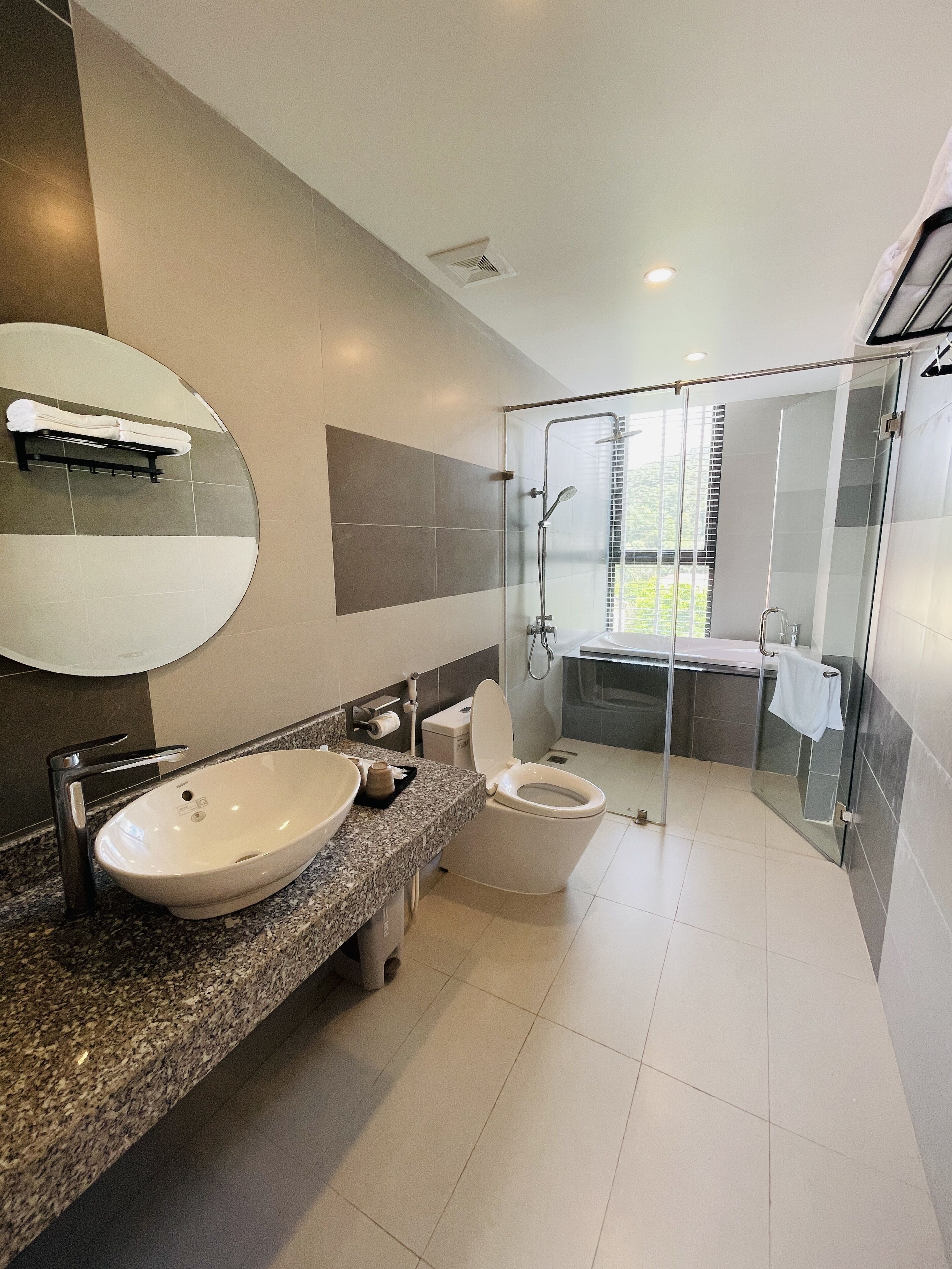 Une salle de bain moderne avec un comptoir en granit, un lavabo blanc, des toilettes et une douche à parois de verre.