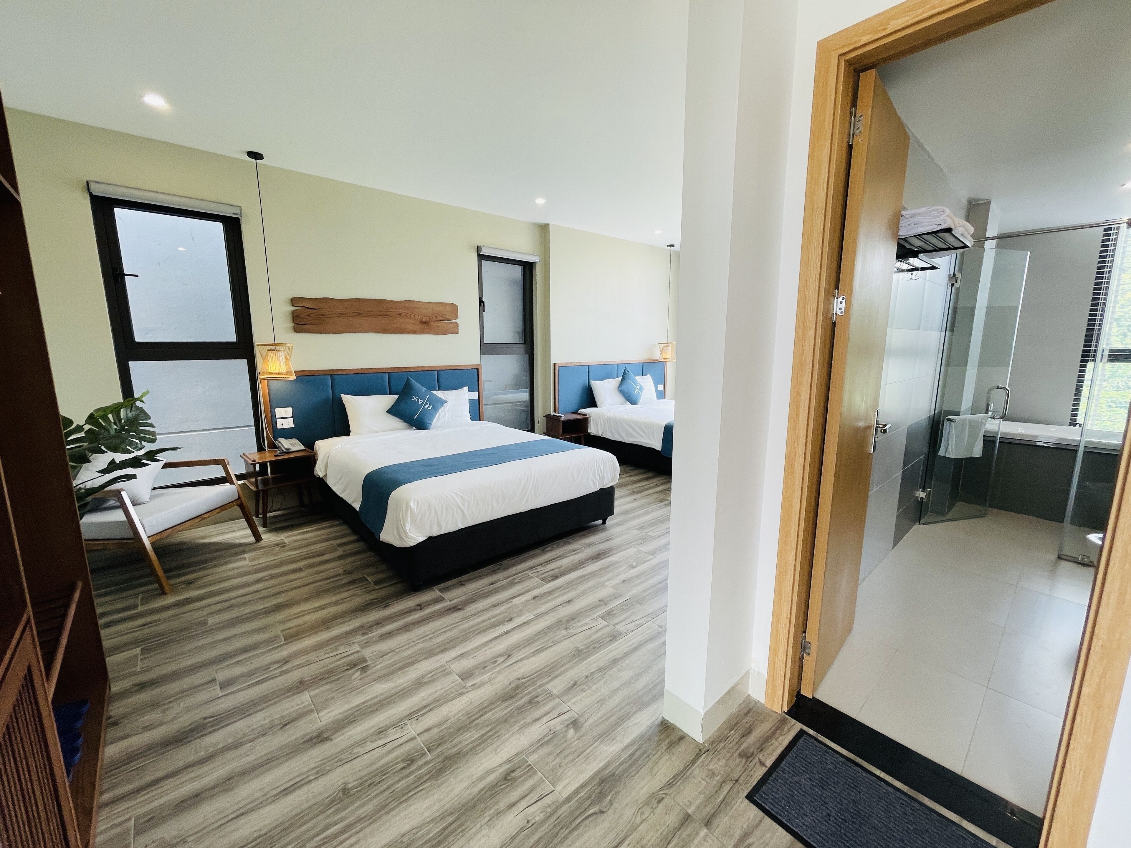 Une chambre d’hôtel avec un grand lit, deux tables de chevet, un bureau, une chaise, une plante en pot et un espace douche.