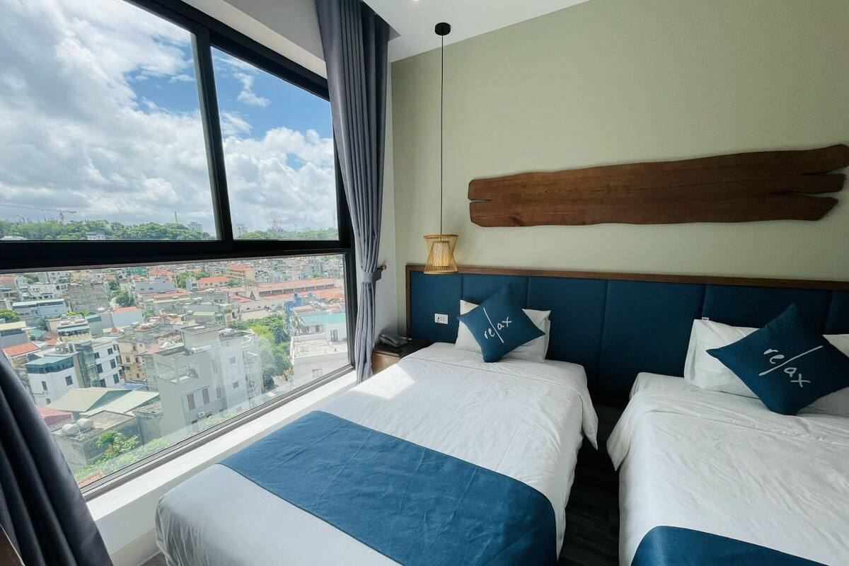 Habitación de hotel con dos camas, un ventanal grande con vista a la ciudad y cabecero de madera.