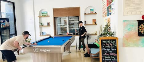 A pool table in a room with a dartboard and a chalkboard sign advertising tours and dining options.