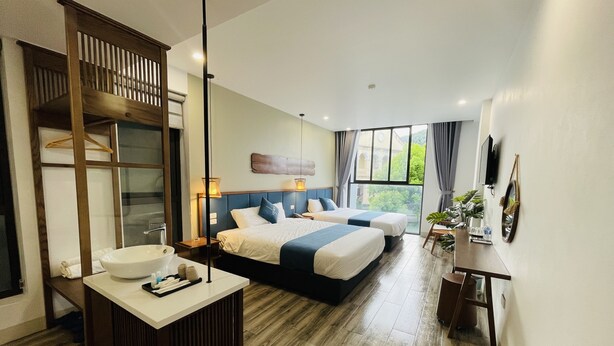 A hotel room with a large bed, a bedside table, a desk with a chair, a large window, and a TV mounted on the wall. - The Light Hotel (Bai Chay)