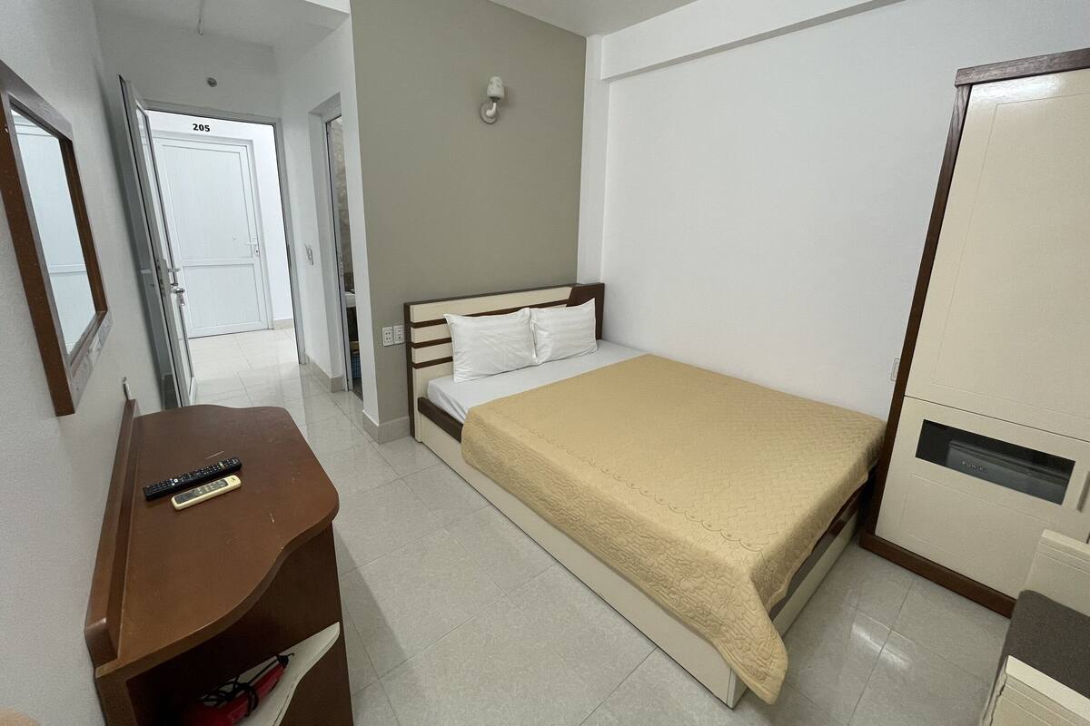 Habitación de hotel con cama, escritorio con silla, armario y baño visible a través de una puerta abierta.
