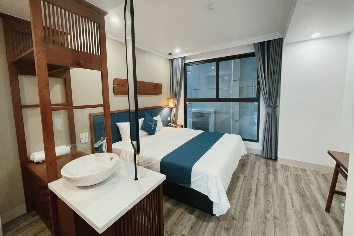 Una habitación de hotel con cama, mesita de noche y un ventanal grande.