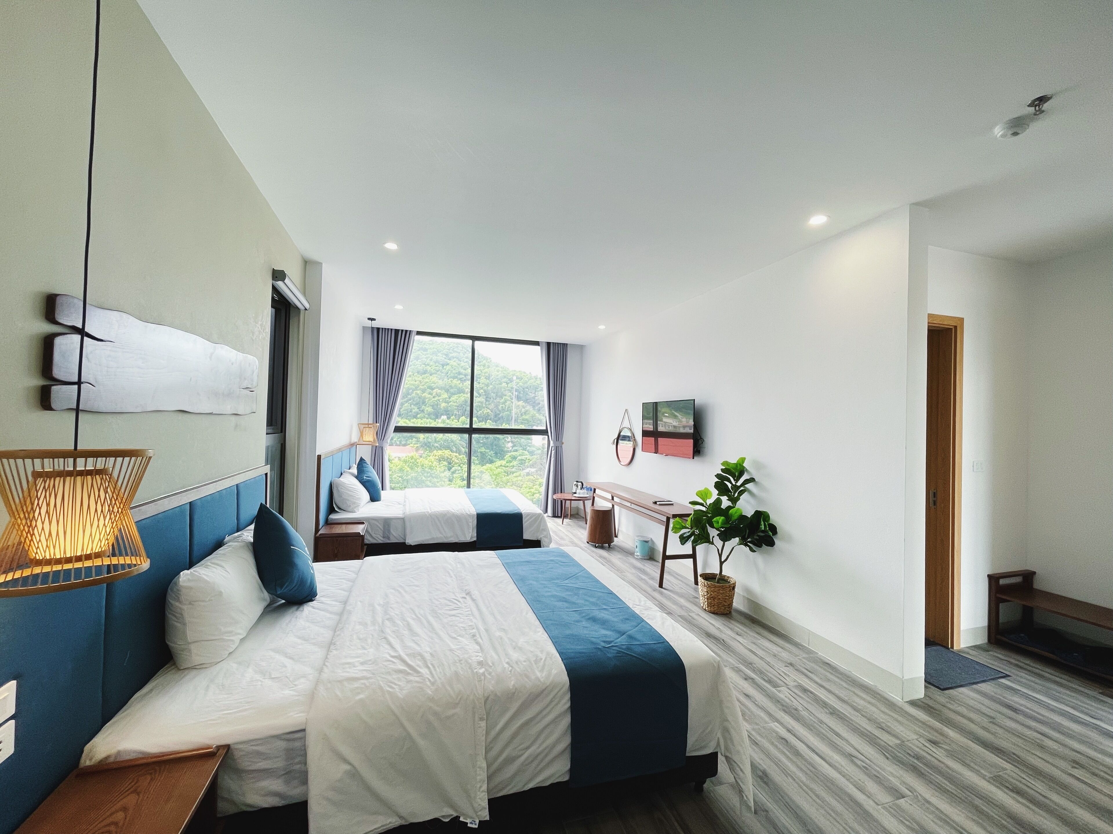 A modern hotel room with two beds, a large window, a dining table, and a plant.