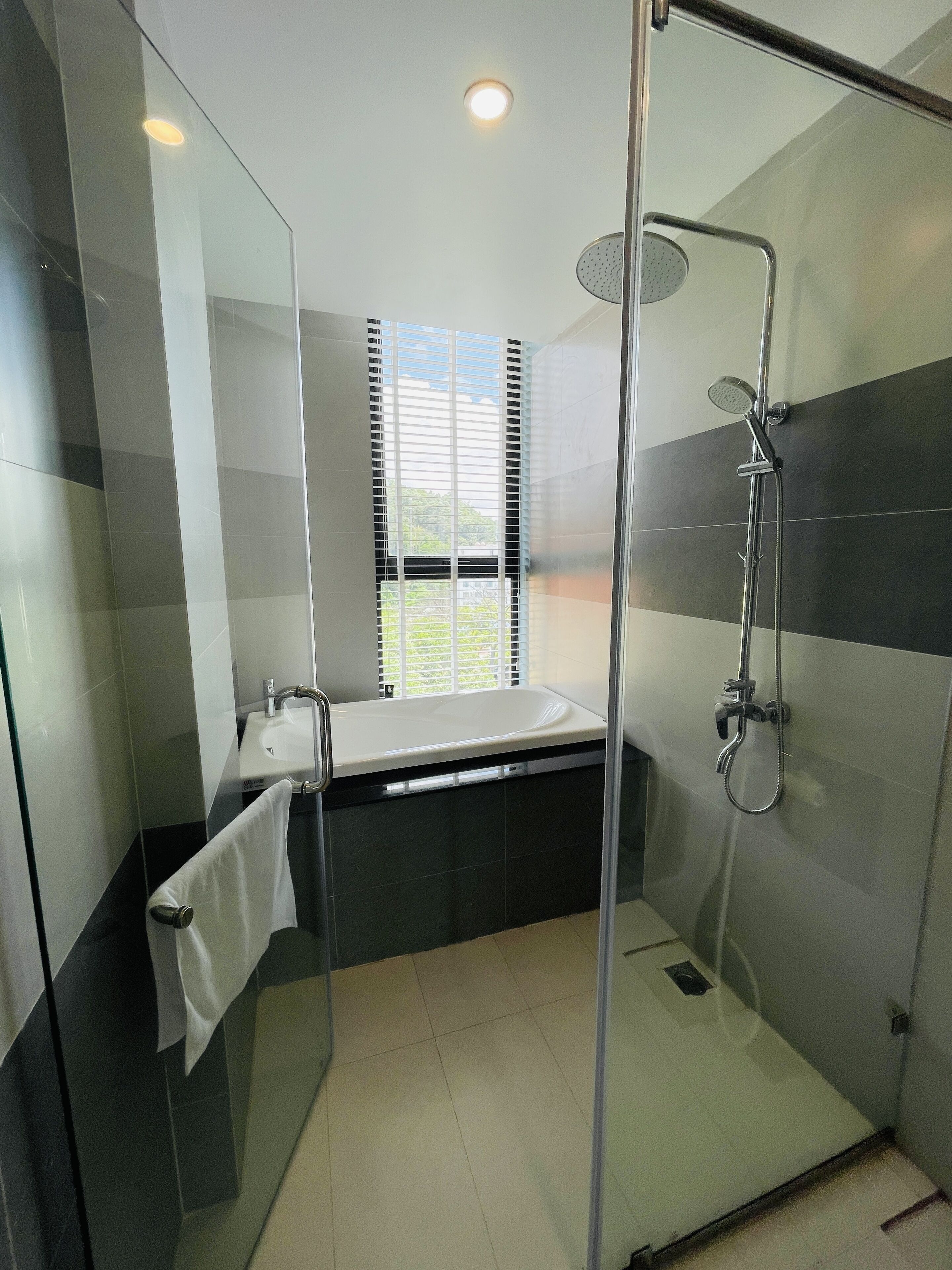 A modern bathroom with a glass shower enclosure, a bathtub, and a window with blinds.