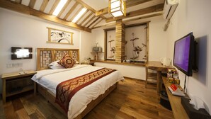 A bedroom with a wooden bed, a television, a desk with a computer, and a window with a view of flowers. - Zhangjiajie Wang Yi Inn (Zhangjiajie)