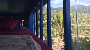 Una habitación con cama, ventanas amplias y vistas a palmeras y colinas.