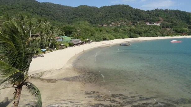 Una playa con agua cristalina, una orilla arenosa y colinas verdes al fondo.