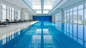 An indoor swimming pool with clear blue water, sunlit from above, and a city view through large windows. - Landison Plaza Hotel Ningbo (Ningbo)