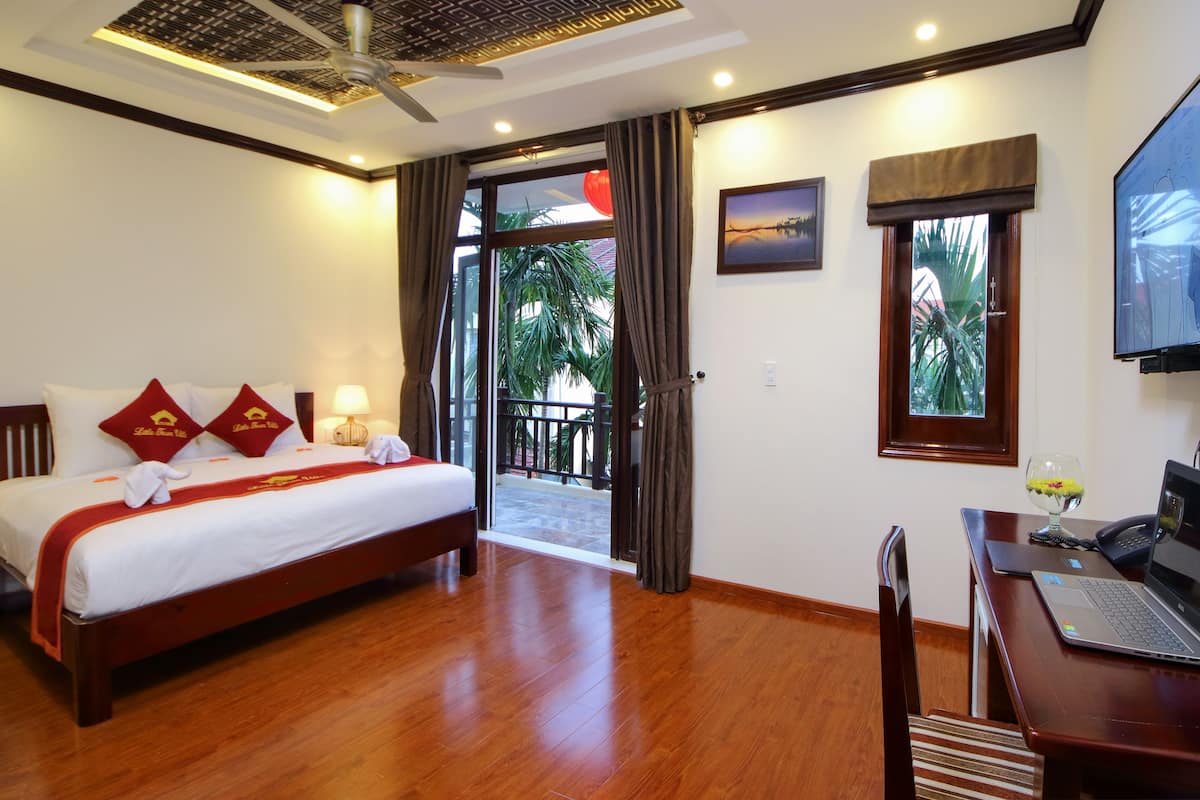A hotel room with a bed, a desk with a laptop, a chair, a ceiling fan, and a view of the outdoors.