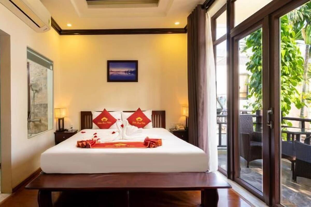 A hotel room with a bed, a bathroom, a large window, and a view of greenery outside.