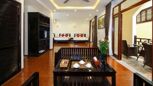 A hotel room with a wooden floor, a ceiling fan, two beds with red and white bedding, a dining table with a vase of flowers, and a view of the outside balcony. - Little Town Villa (Da Nang)