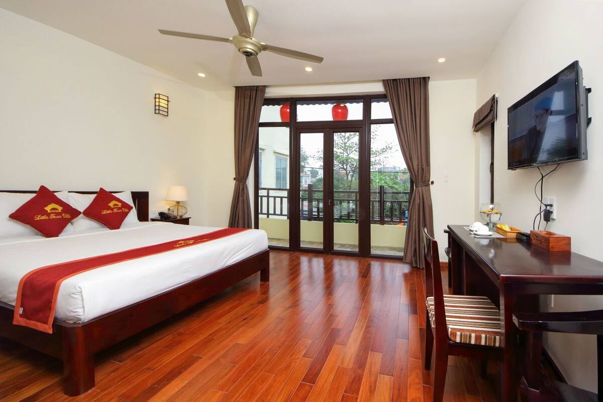 A hotel room with a bed, a desk, a chair, a television, and a balcony with curtains.