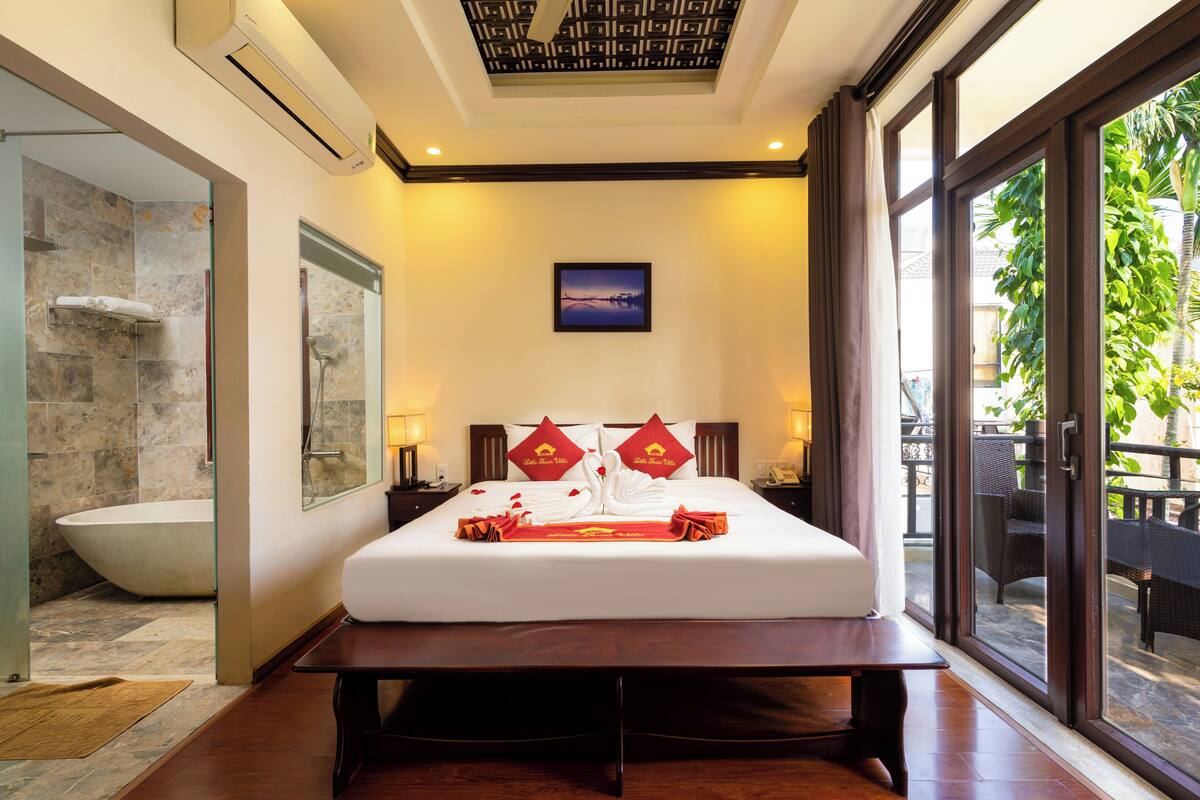 A modern hotel room with a large bed, a bathtub, and a view of the outdoors.