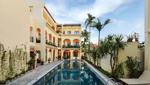 A swimming pool with a clear view of the surrounding buildings, including a multi-story structure with balconies and a covered area. - Little Town Villa (Da Nang)