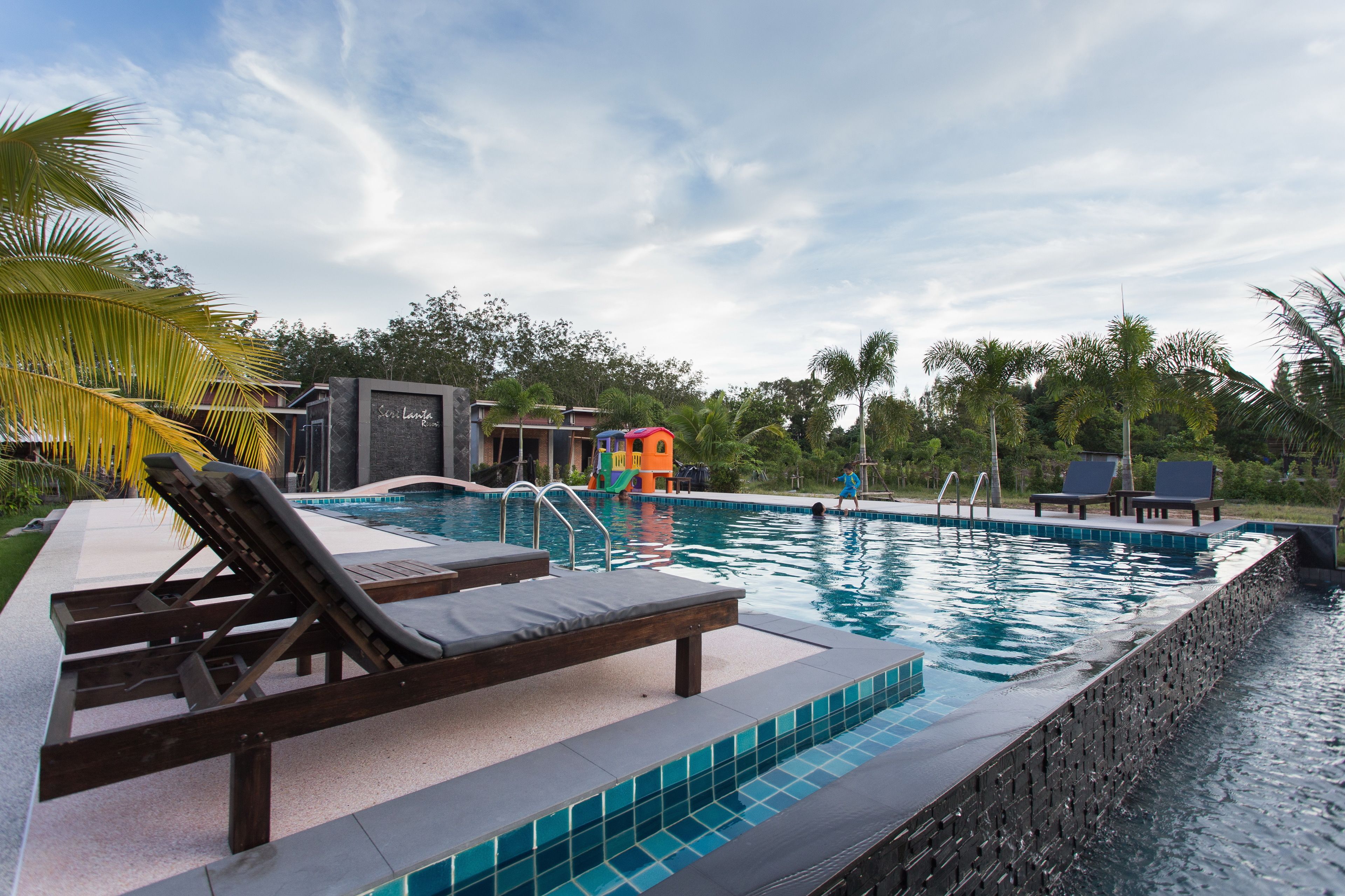 A swimming pool with lounge chairs, a water slide, and palm trees.