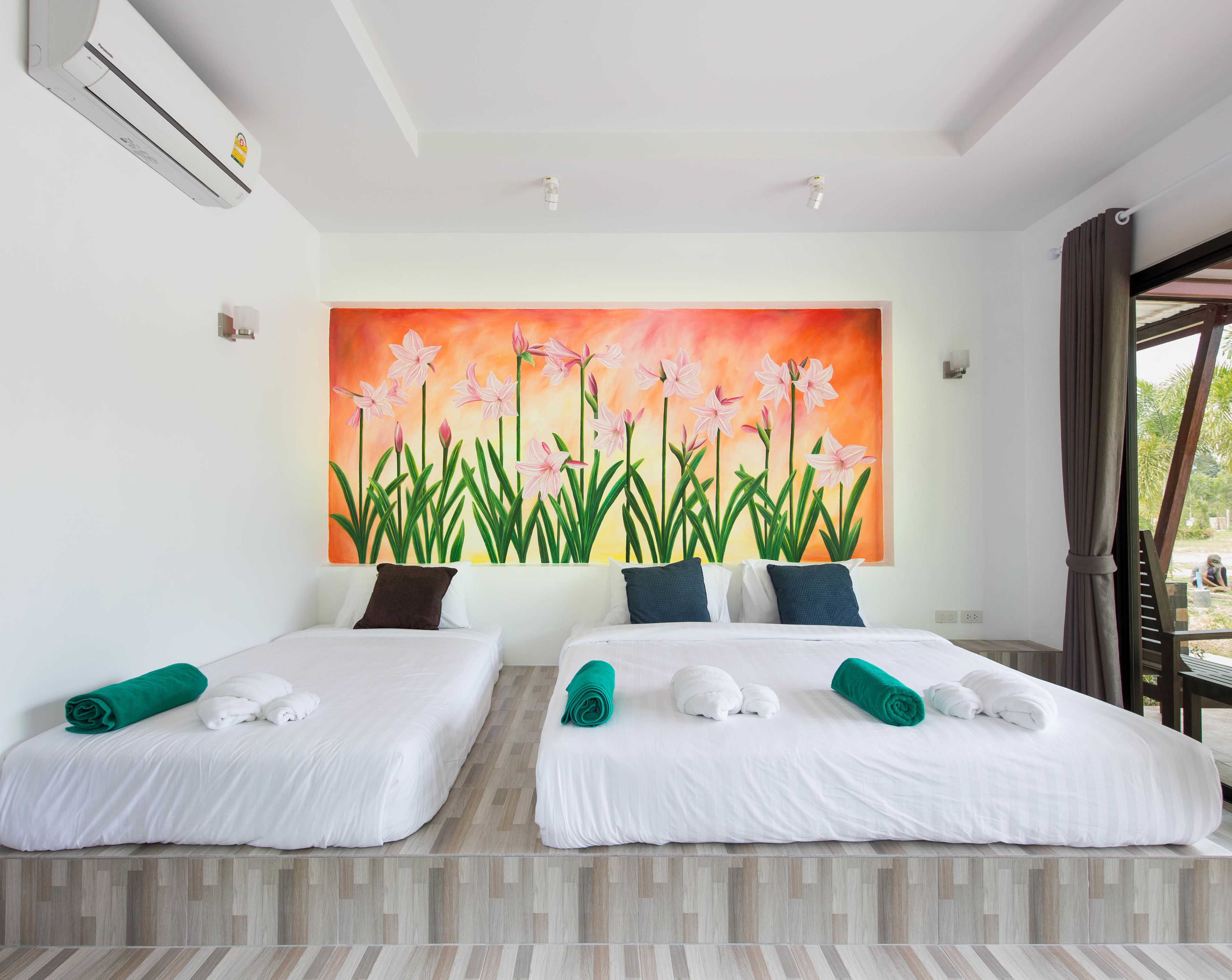 A hotel room with two beds, a large floral painting on the wall, and a view of the outdoors through a window.