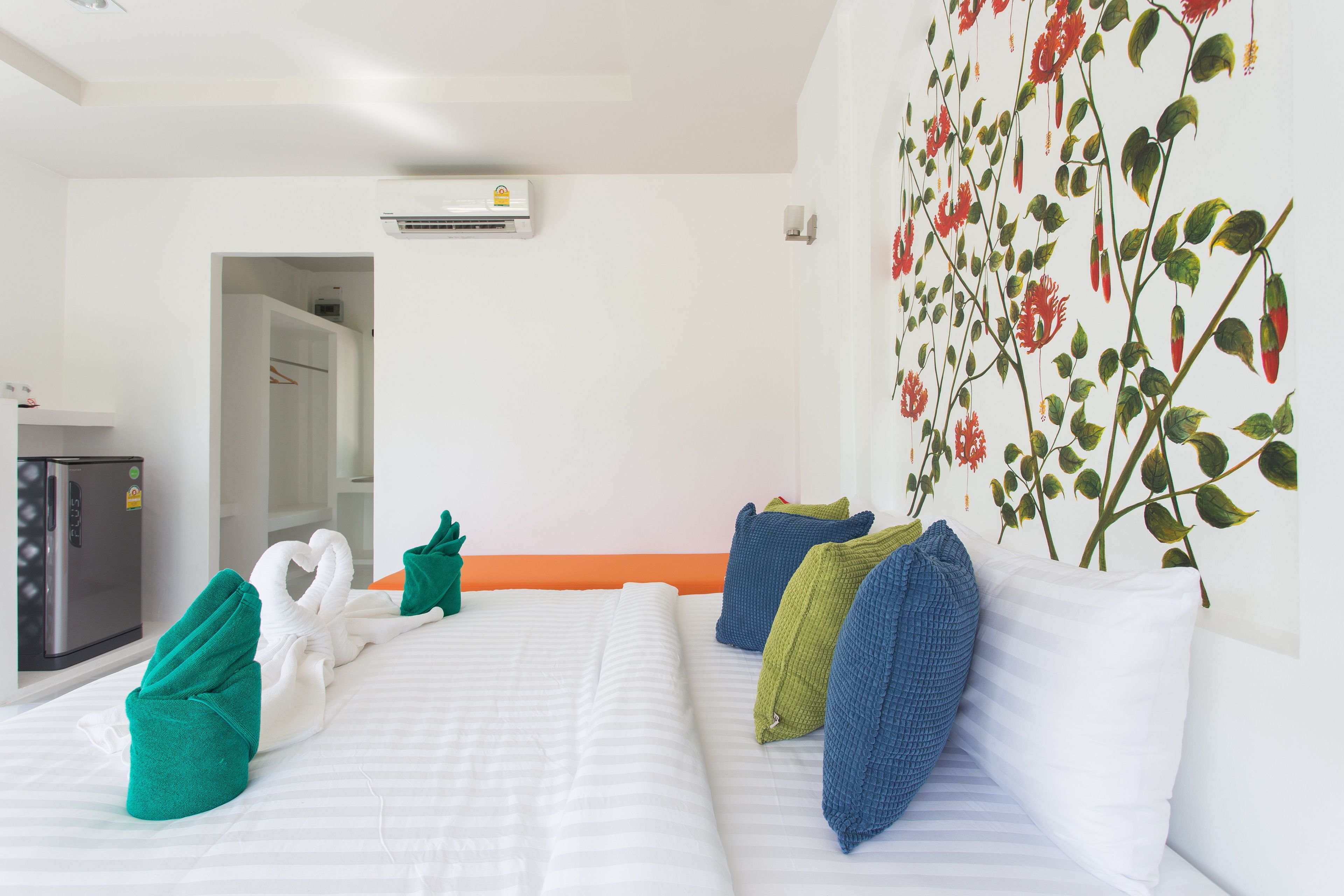 A hotel room with a bed, pillows, a wall-mounted air conditioner, a wardrobe, and a refrigerator.