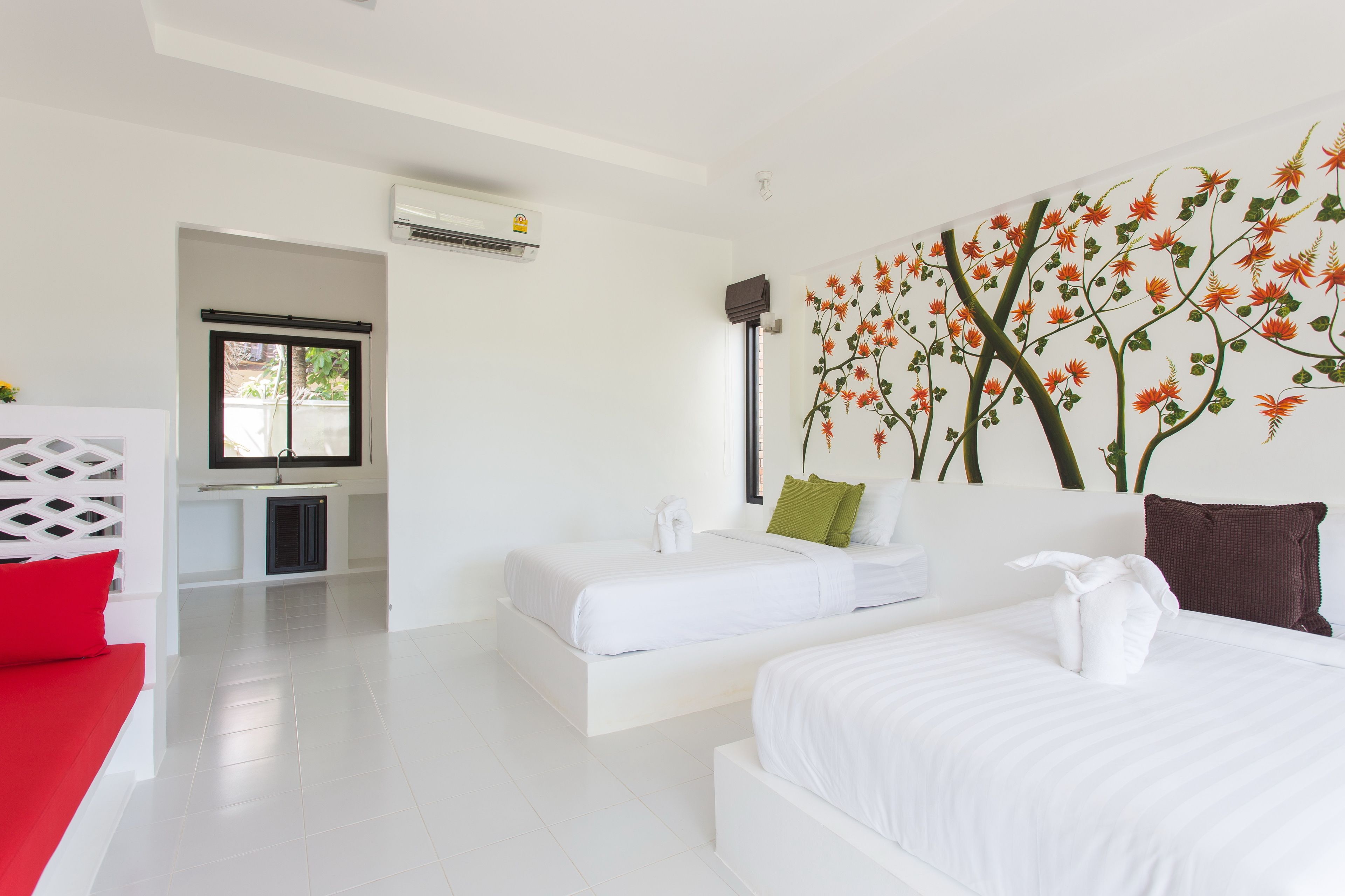A modern hotel room with two beds, a red sofa, a kitchen area, and a wall mural.