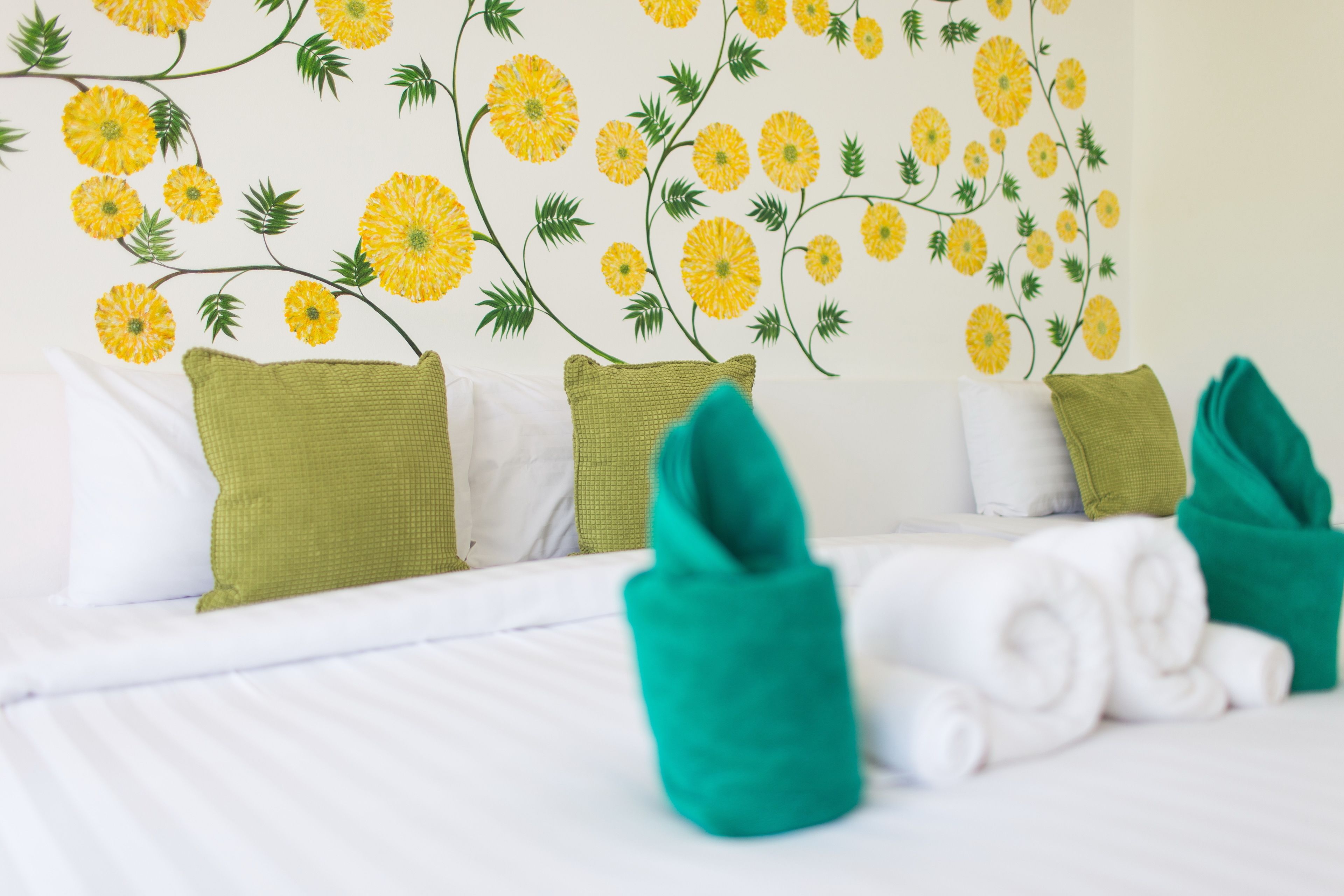A hotel room with a bed, green and white pillows, and a wall with a floral mural.