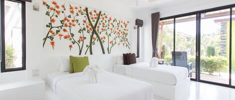 A modern hotel room with a large bed, two white sofas, a wall mural, and a balcony with a view.
