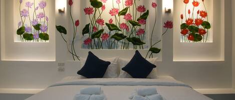 A hotel room with a large bed, two dark blue pillows, and a wall-mounted artwork of pink lotus flowers.
