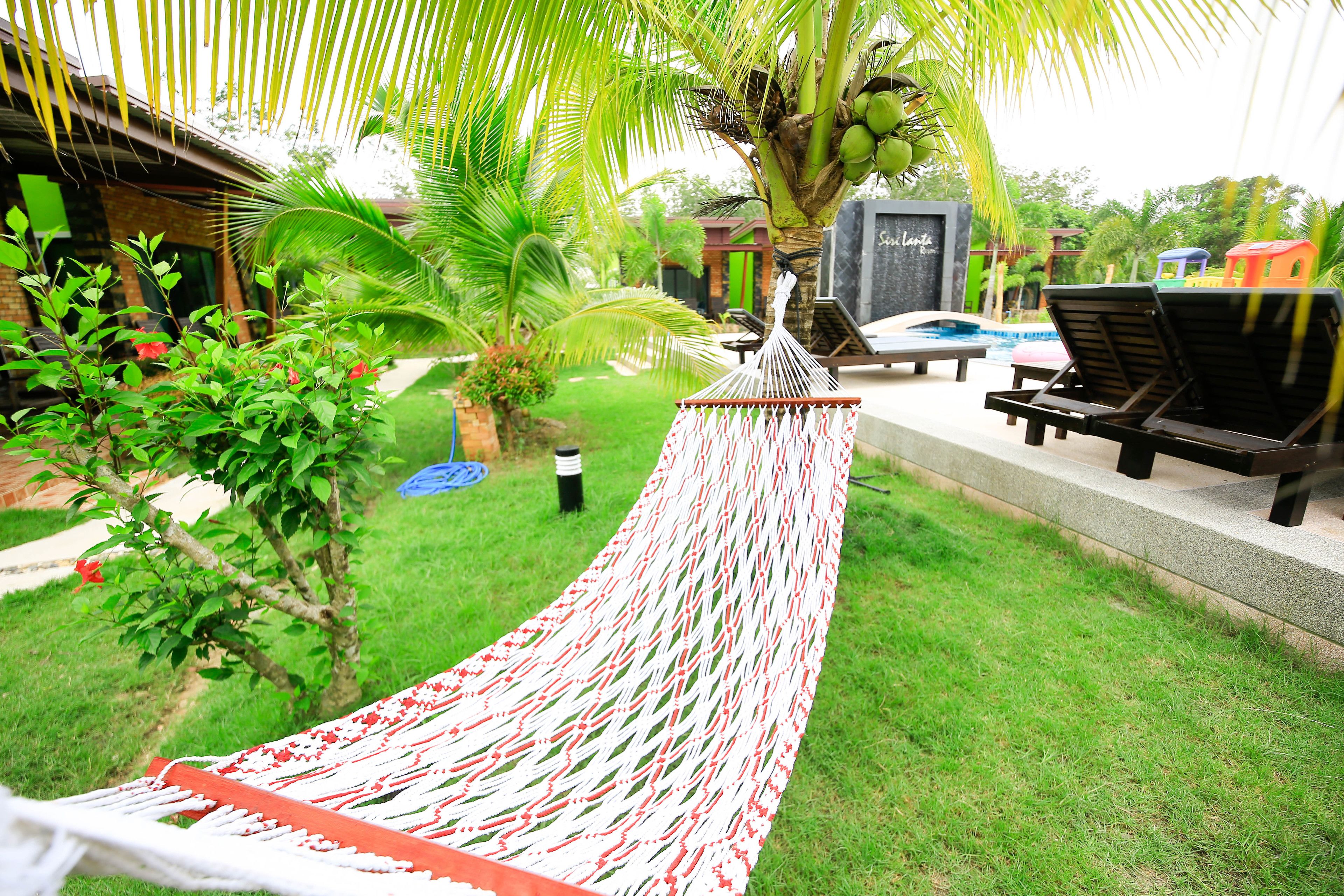 Una hamaca en un jardín con piscina y sillas de descanso.