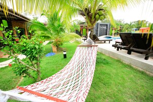 Una hamaca en un jardín con piscina y sillas de descanso.