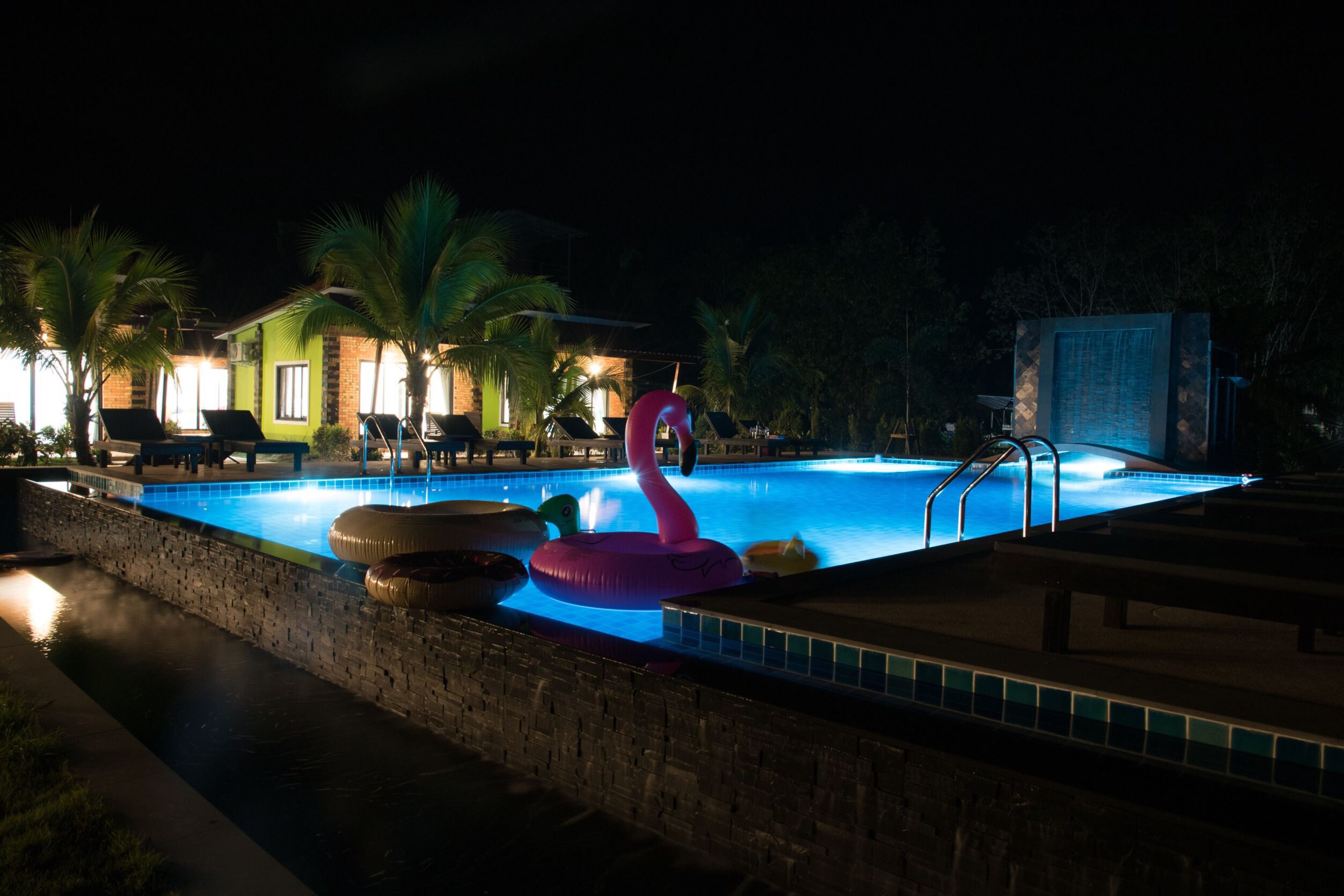 Una piscina con un flotador de flamenco rosa, palmeras y un muro de ladrillo.