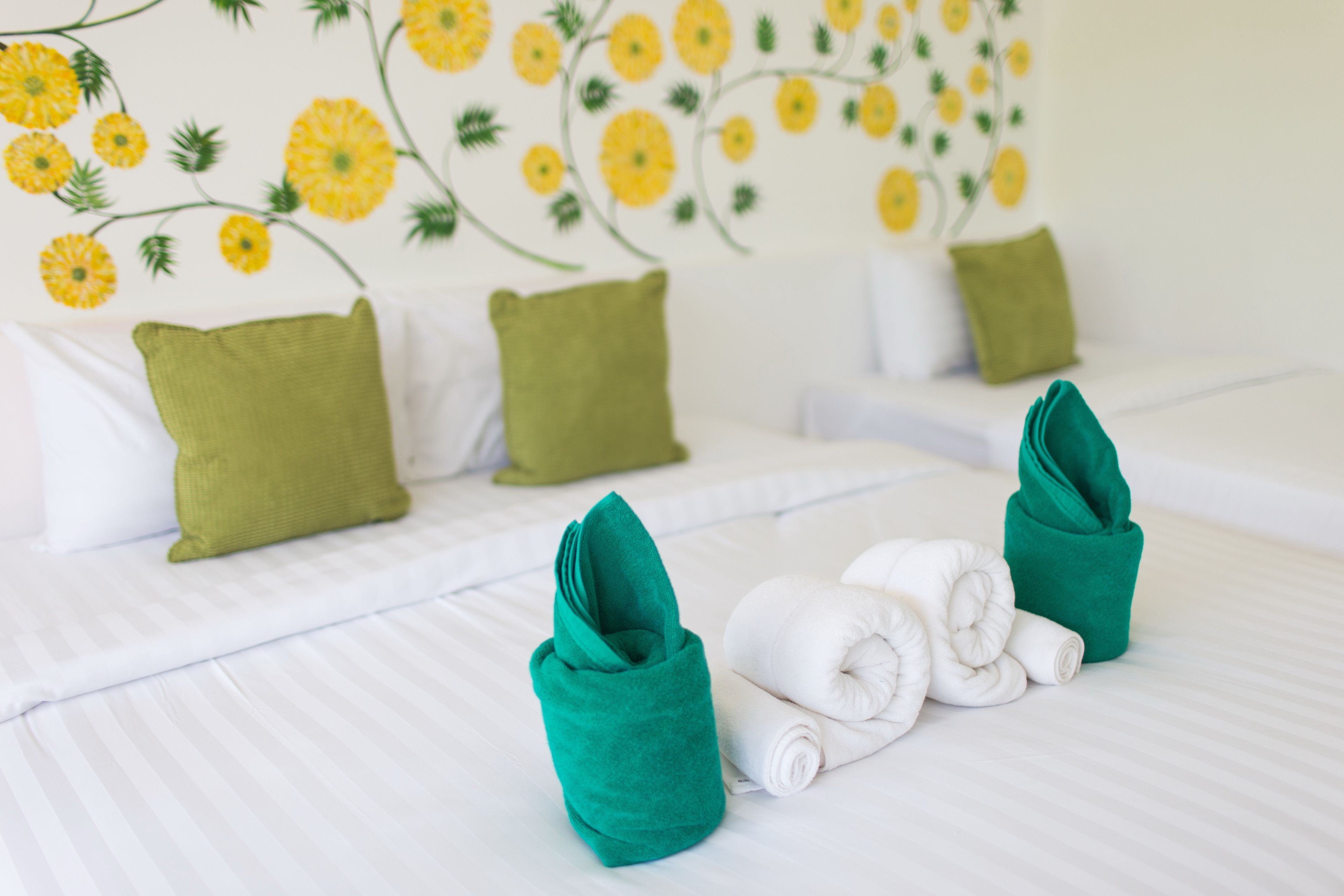 A hotel room with a bed, green pillows, and neatly folded white towels.