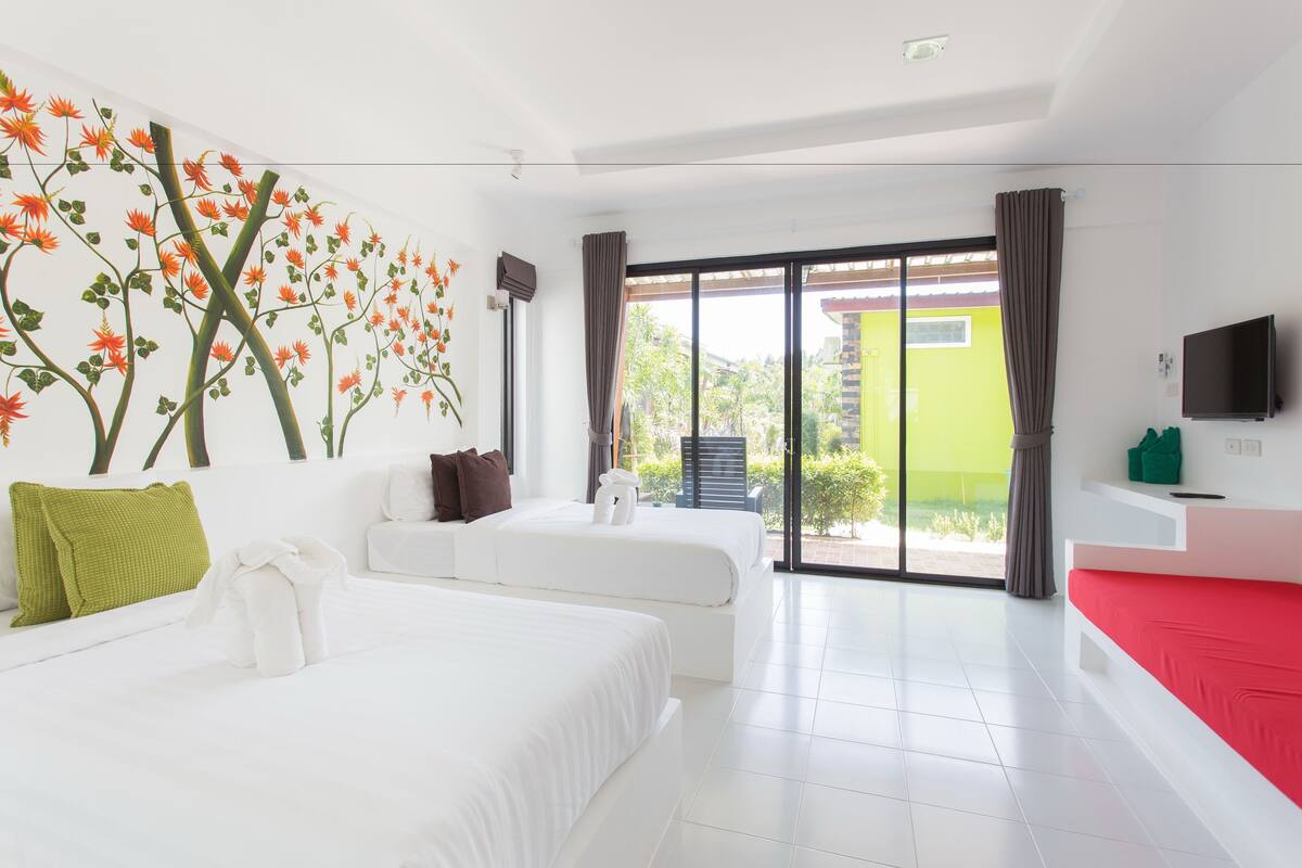 A modern hotel room with two beds, a large window with a view, a flat-screen TV, and a red accent wall.
