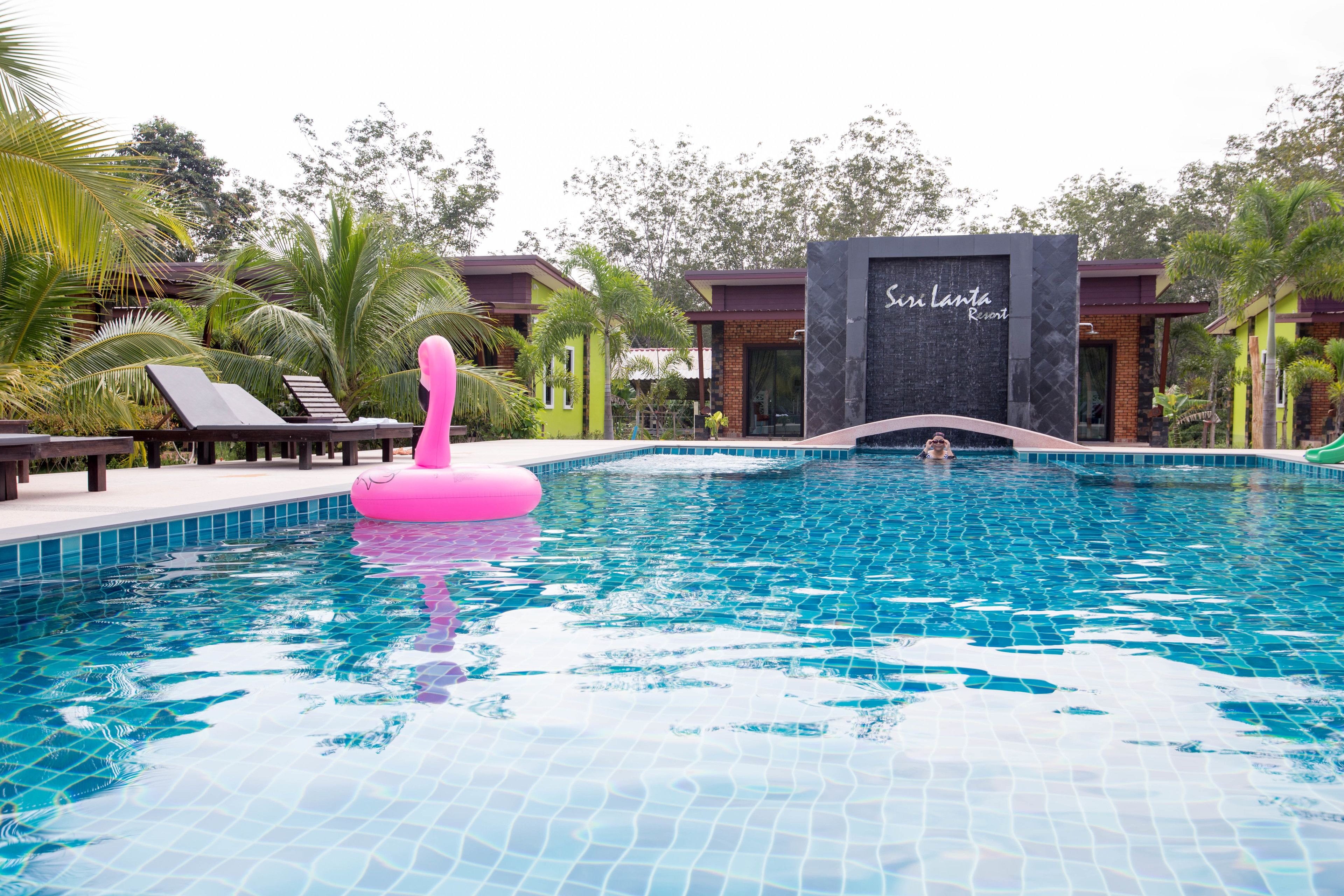 A swimming pool with a pink floatation device, lounge chairs, and a building labeled "Sun Lanta Resort".