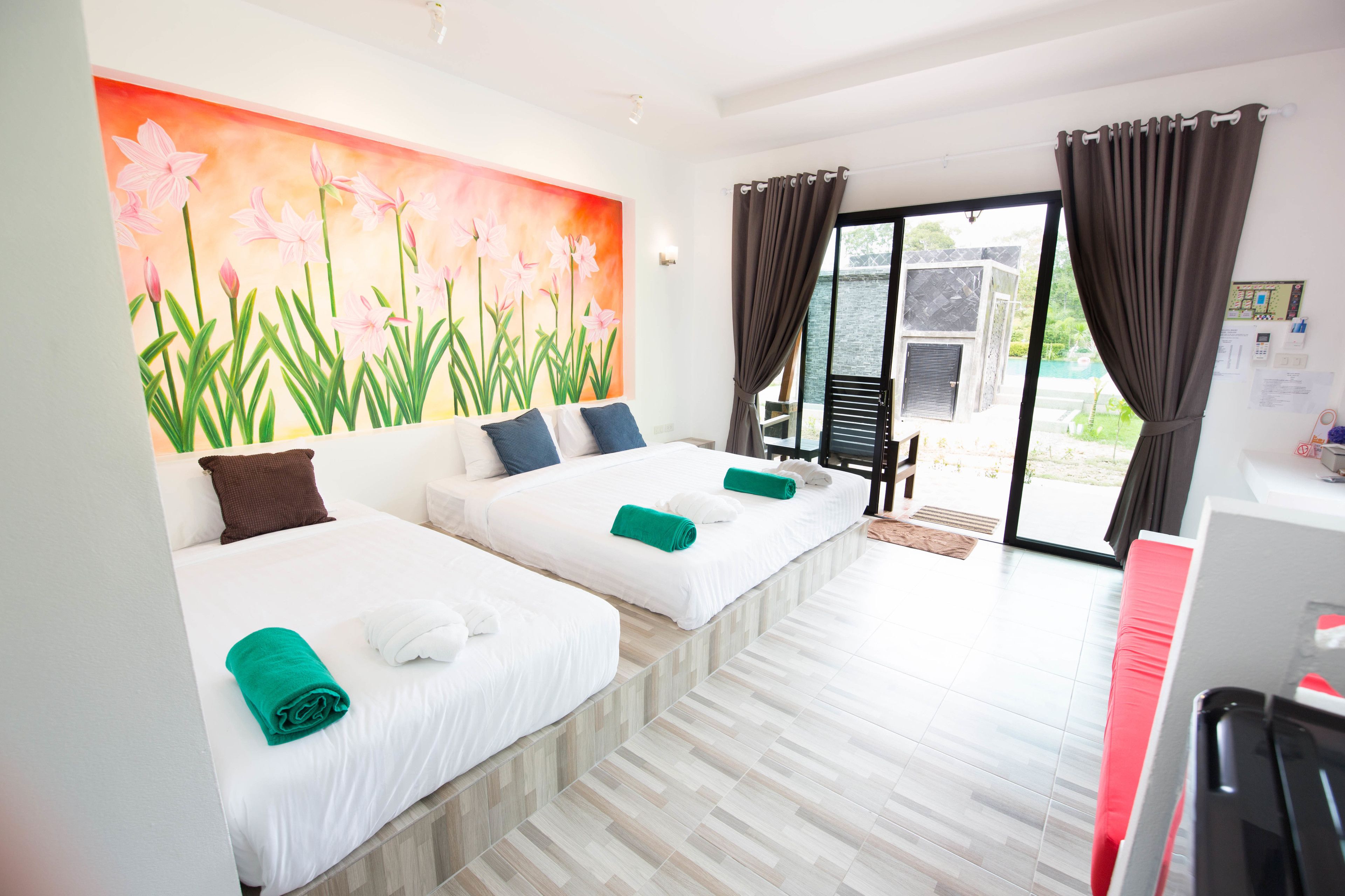 Une chambre d’hôtel avec deux lits, un tableau de fleurs accroché au mur, une vue sur l’extérieur par une porte coulissante et un bureau avec un ordinateur.