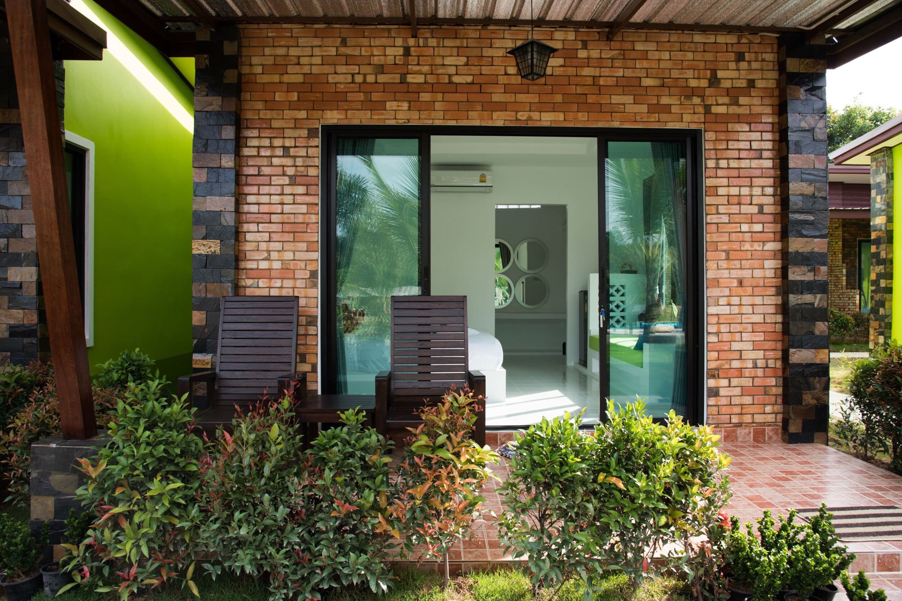 Een modern gebouw met een bakstenen gevel, grote glazen schuifdeuren en een klein terras met twee houten stoelen en potplanten.