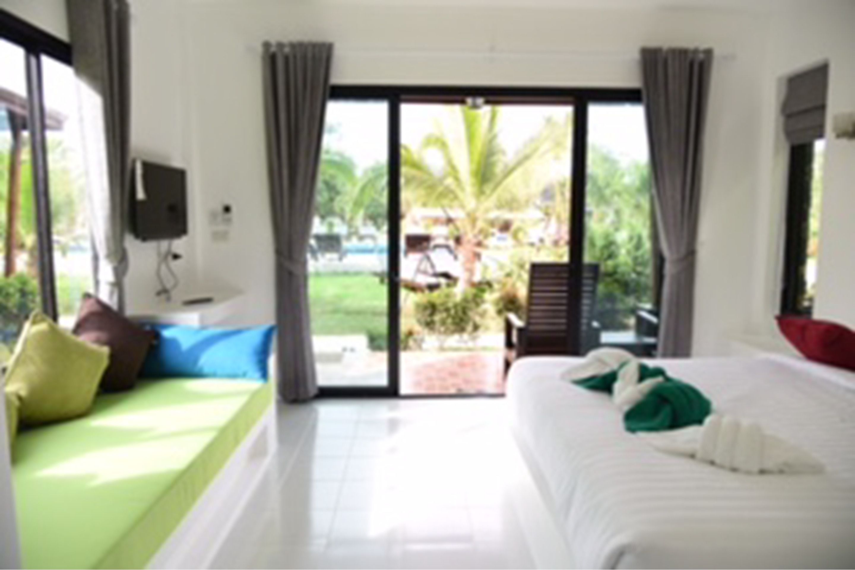 A hotel room with a bed, a green sofa, a TV, and a view of the outdoors.