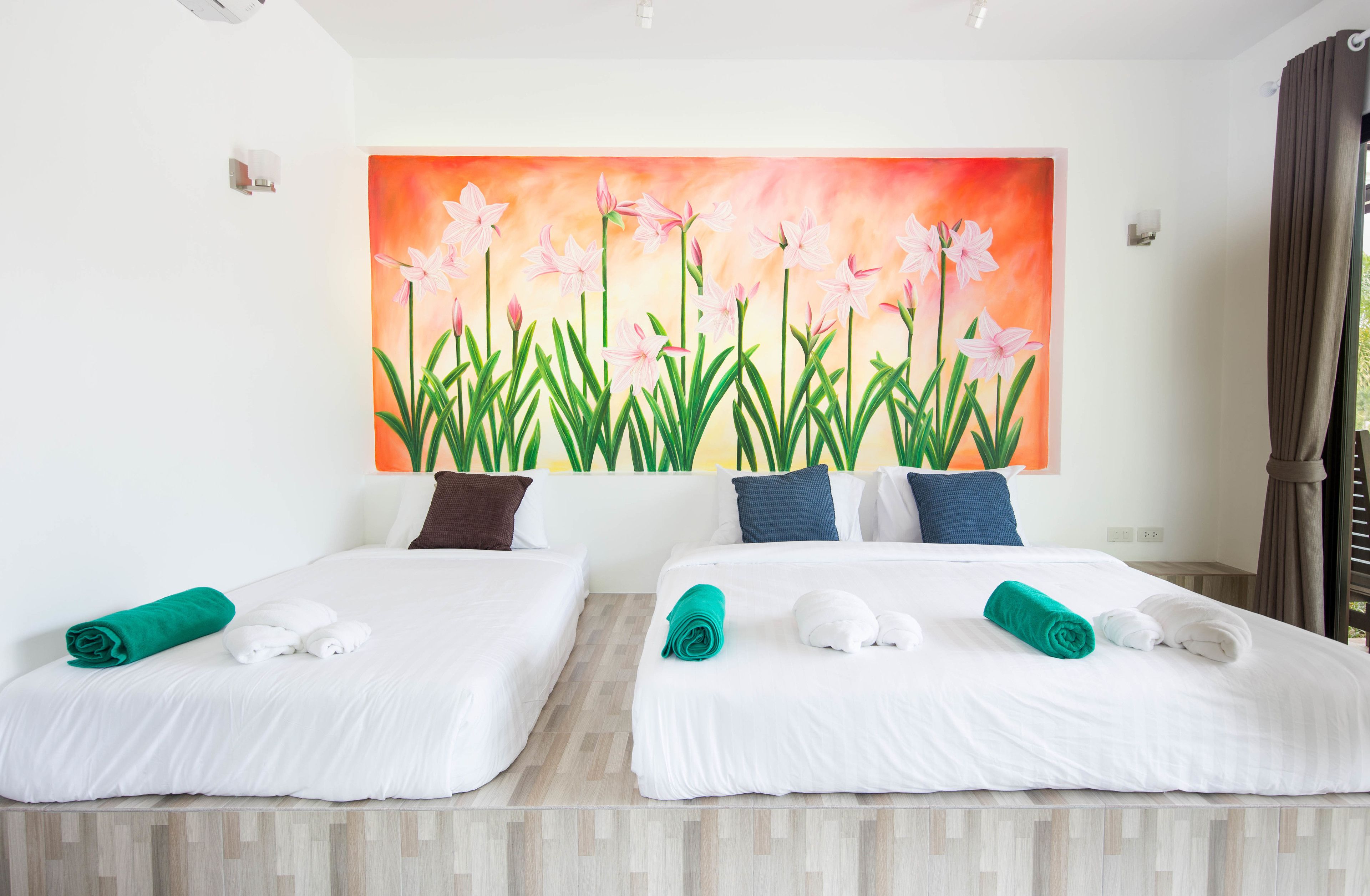 Een hotelkamer met twee bedden, witte beddengoed, blauwgroene handdoeken en een groot bloemschilderij aan de muur.