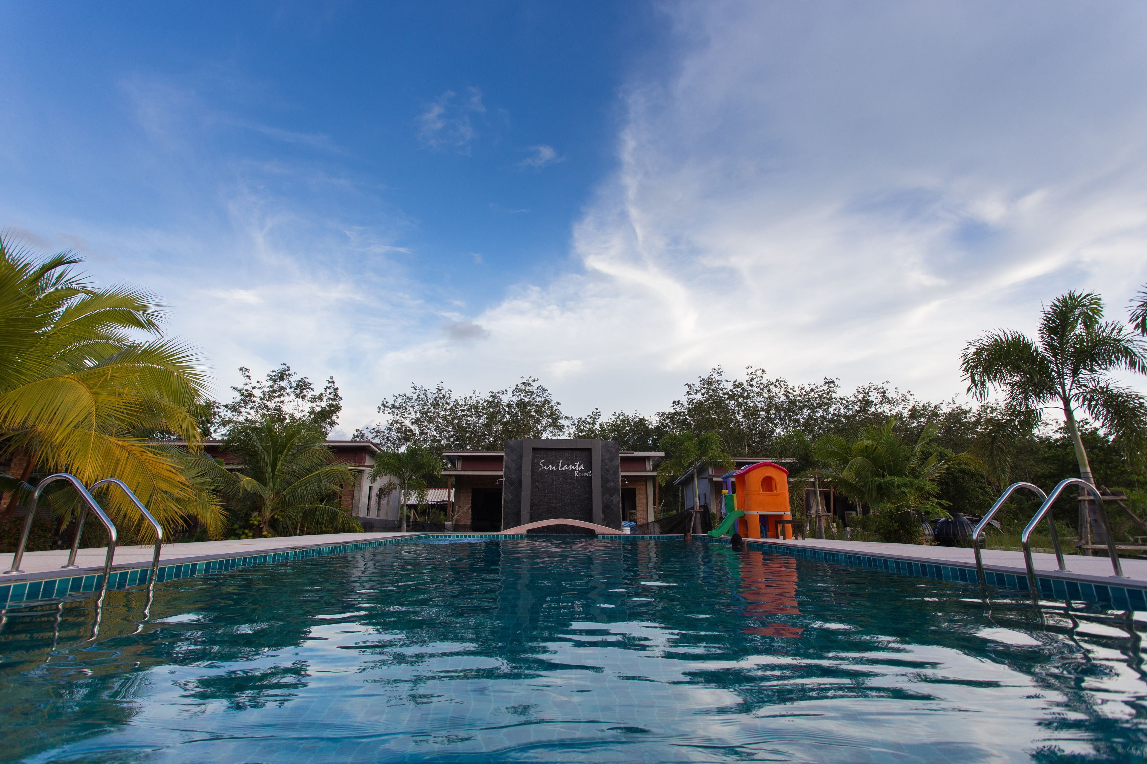 A swimming pool with a clear blue sky, palm trees, and a building with a sign that reads "Sea Lagoon".