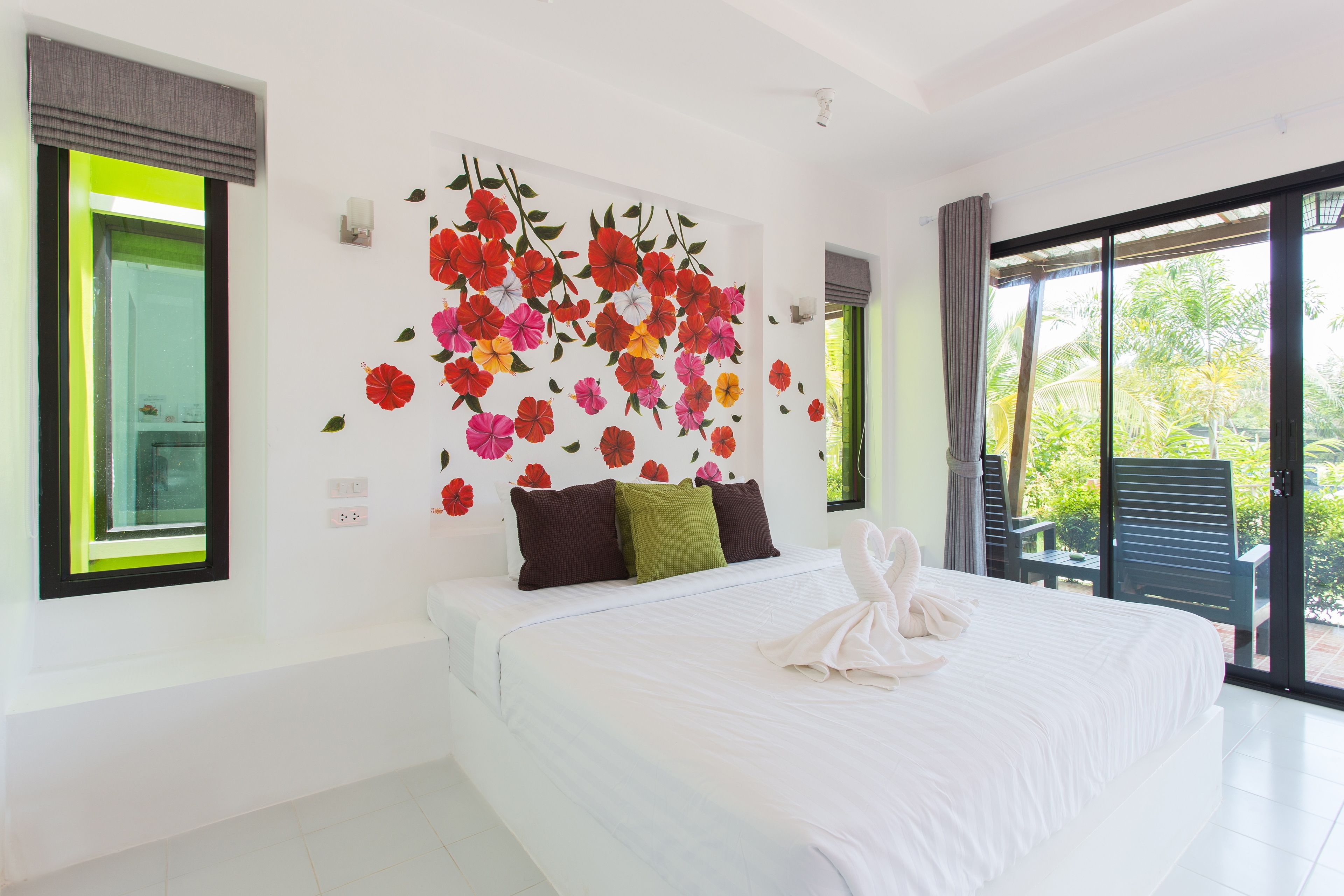 Habitació d'hotel amb un llit gran, un mural floral a la paret i vistes a la vegetació per la finestra.