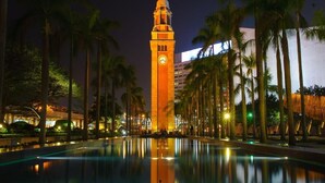 A nighttime view of a building with a clock tower, surrounded by palm trees and a reflecting pool. - Skyview Hostel (Kowloon)