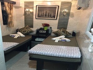 A compact hotel room with two beds, each with patterned bedding and pillows. There is a small table with a telephone and a vase with flowers. A framed picture hangs on the wall above the beds. - Skyview Hostel (Kowloon)