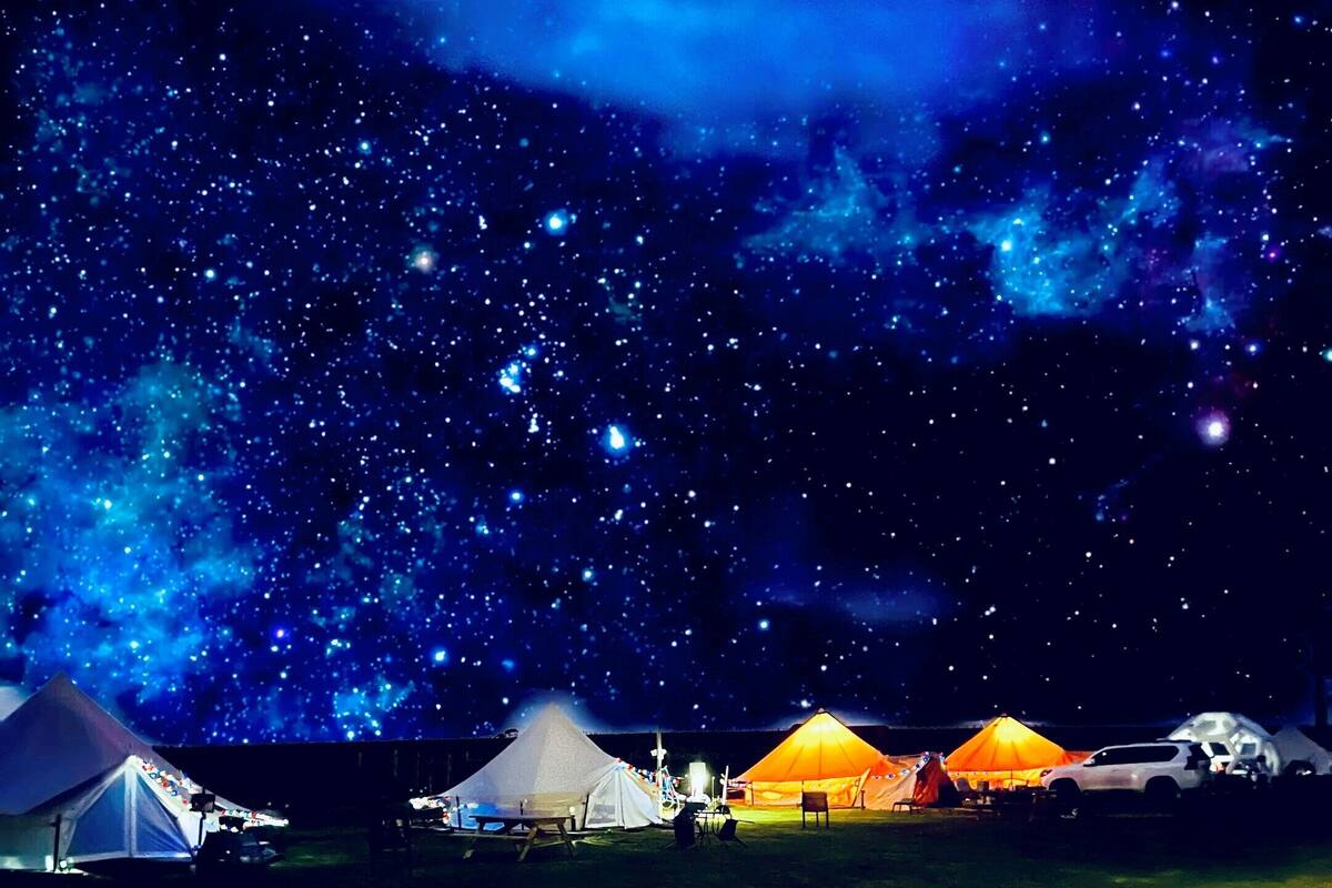 Cielo estrellado con varias tiendas de campaña iluminadas con luz artificial.