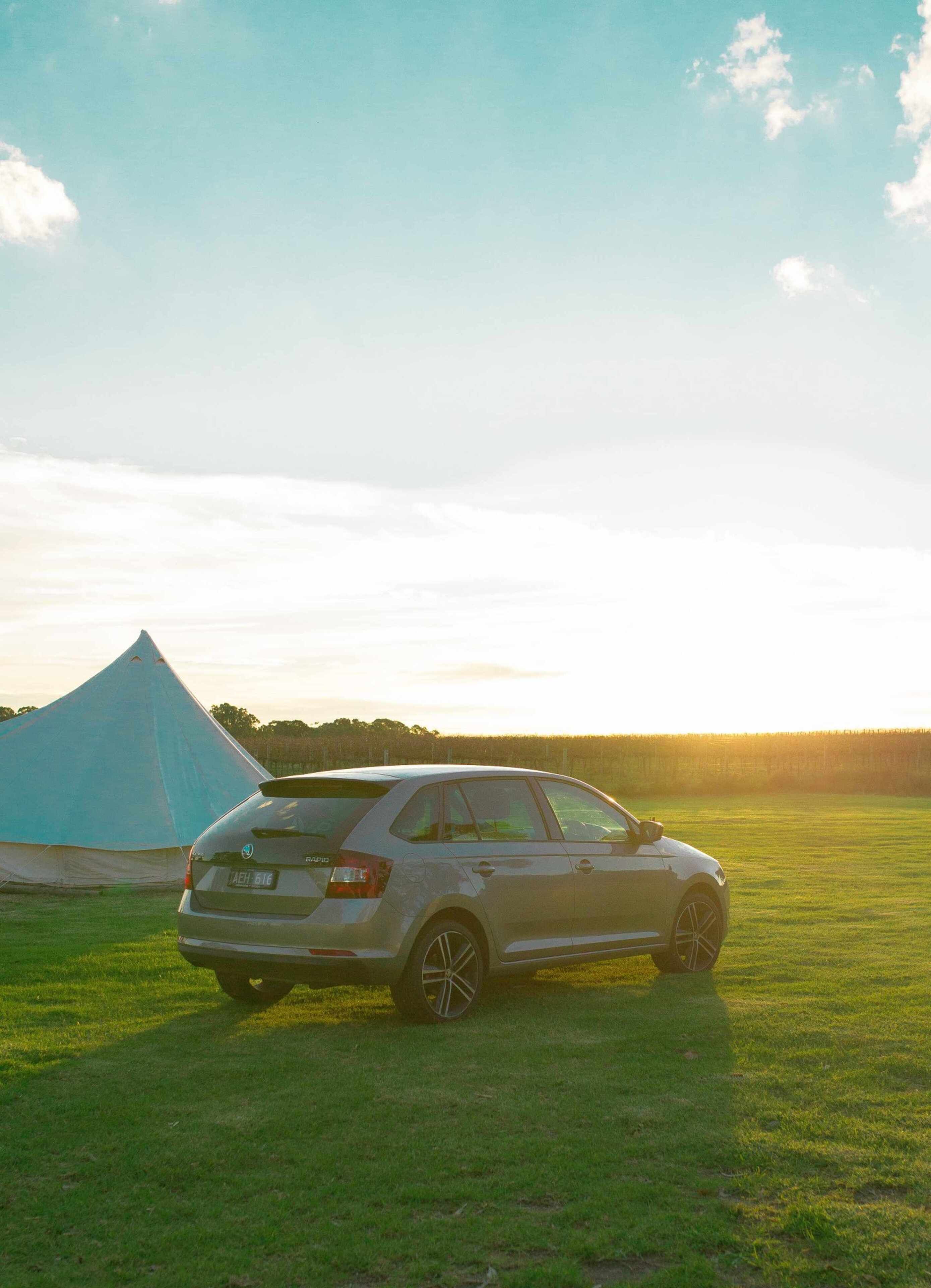 A silver car parked in a grassy field with a blue tent in the background.