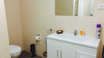 Un baño con inodoro, lavamanos, espejo y un cubo de basura.